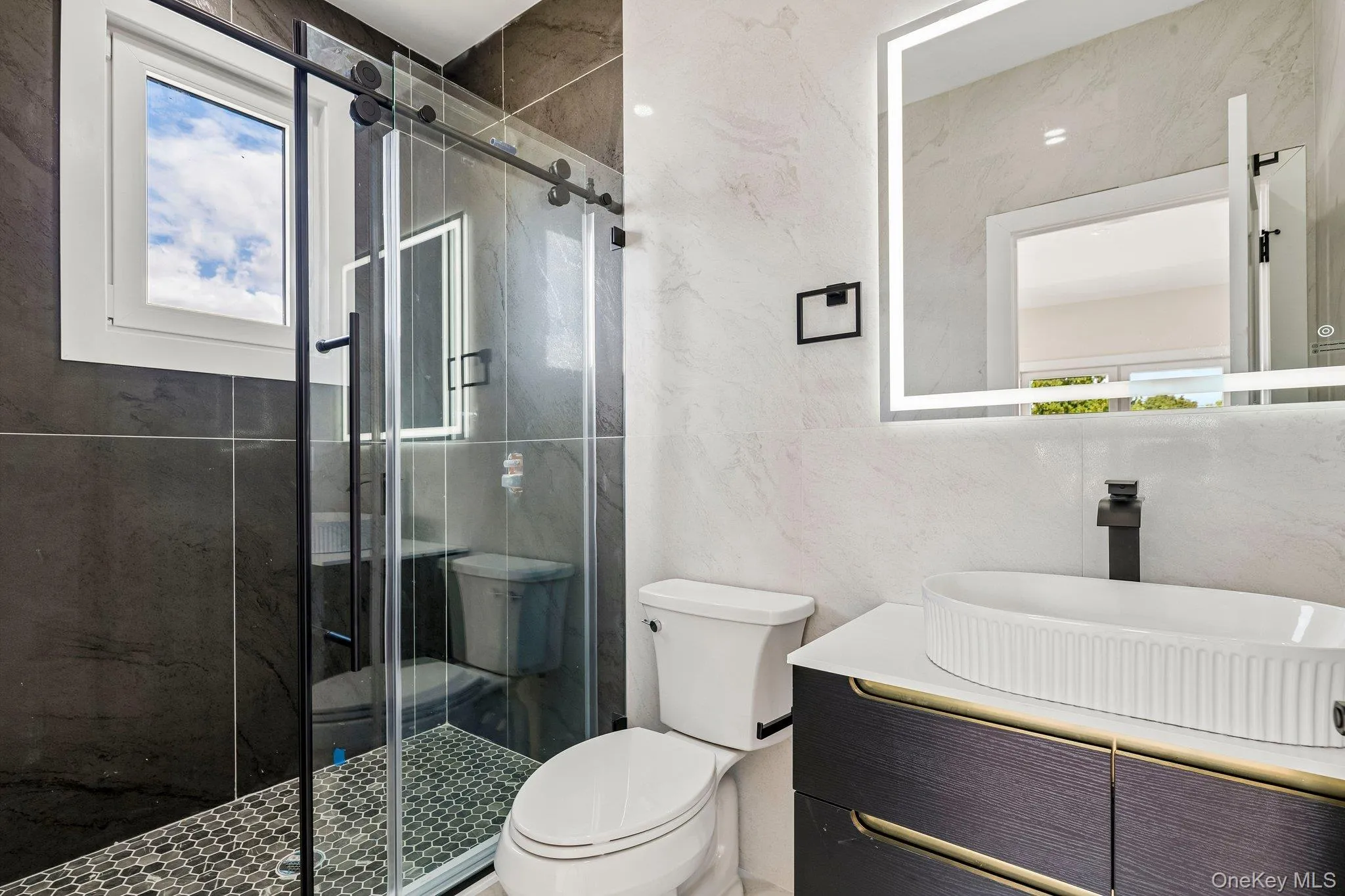 Contemporary bathroom featuring a sliding glass shower door, a large rectangular illuminated mirror, a vessel sink, dark wood-finish cabinetry, and a window Contemporary bathroom featuring a sliding glass shower door, a large rectangular illuminated mirror, a vessel sink, dark wood-finish cabinetry, and a window