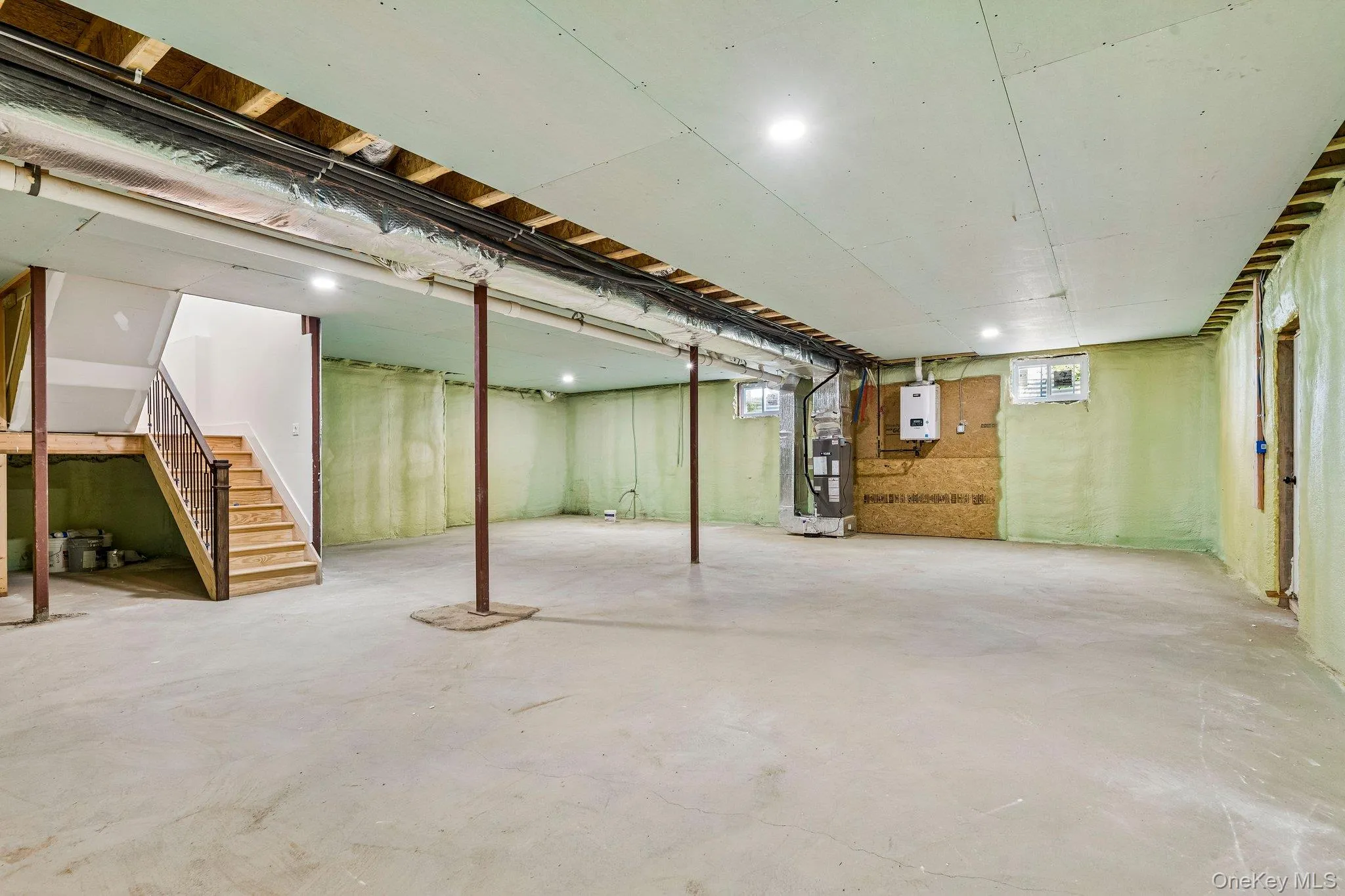 Spacious unfinished lower level with concrete flooring, recessed lighting, exposed ceiling joists, and a finished wooden staircase with railing Spacious unfinished lower level with concrete flooring, recessed lighting, exposed ceiling joists, and a finished wooden staircase with railing