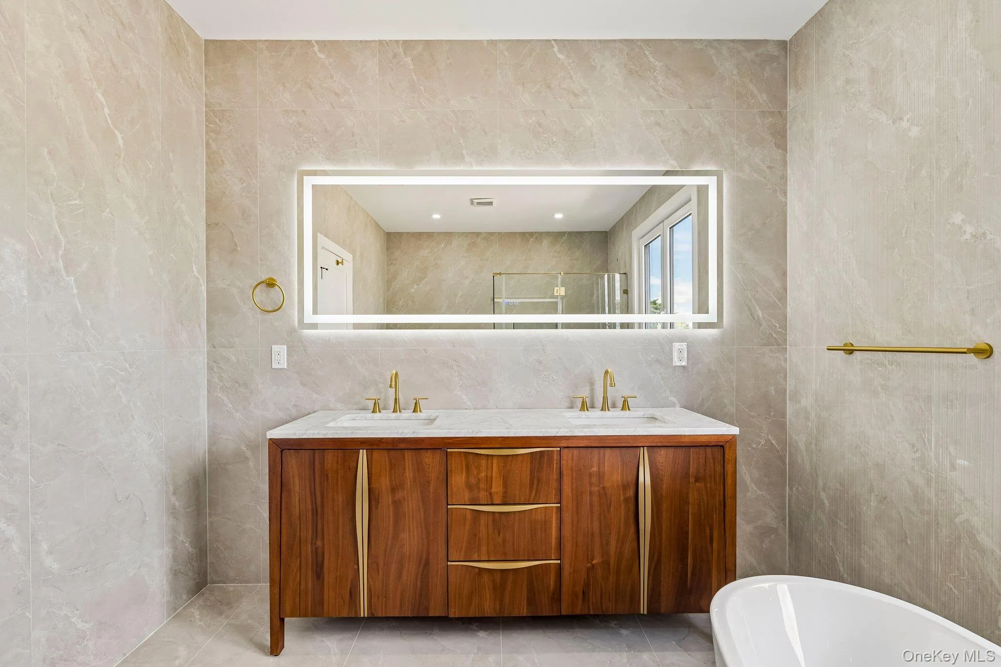 Dual sink vanity with wood-finish cabinetry, integrated countertop, and brass-finish fixtures Dual sink vanity with wood-finish cabinetry, integrated countertop, and brass-finish fixtures