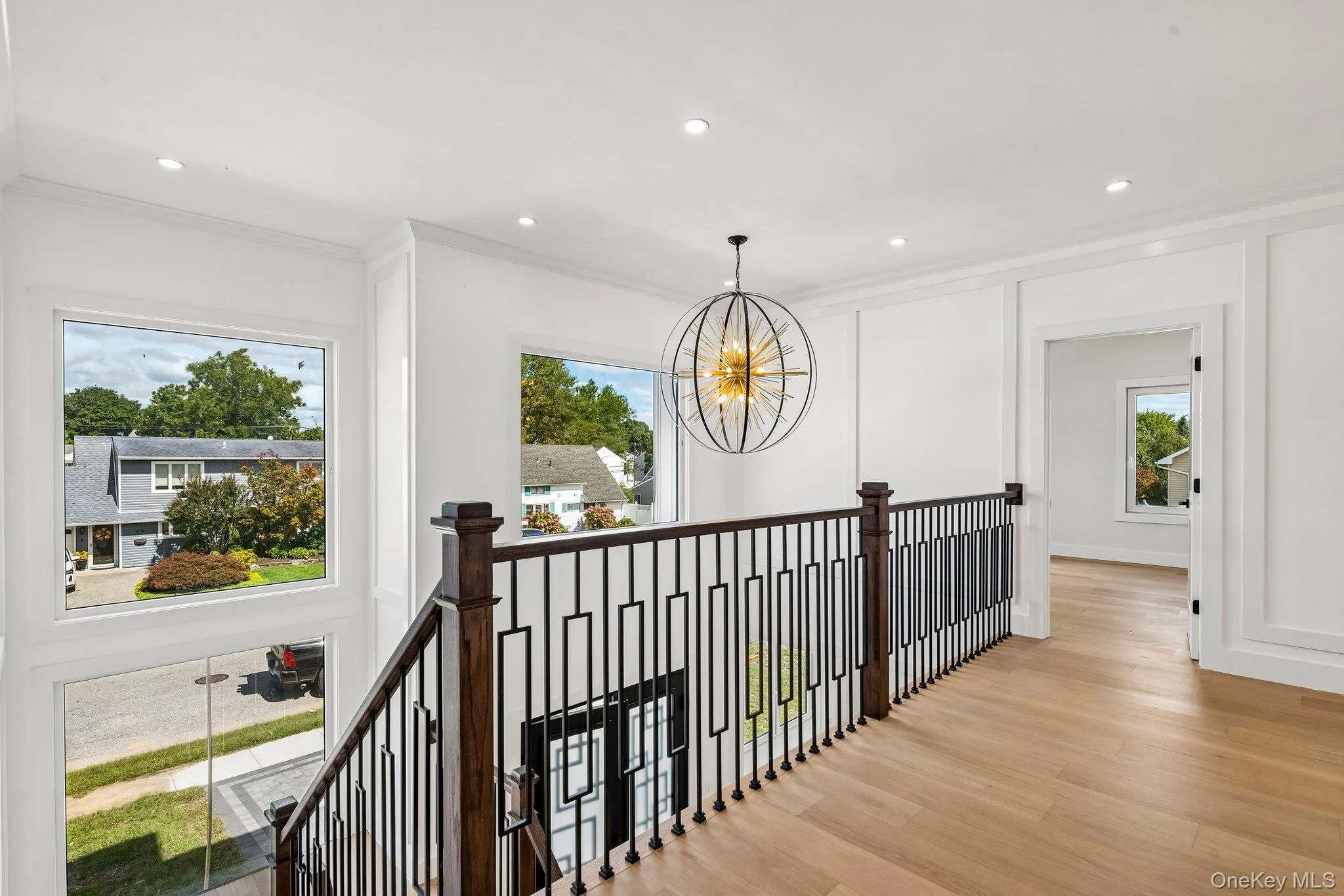 Hardwood flooring, custom iron balusters, recessed lighting, white wall paneling, and an oversized chandelier Hardwood flooring, custom iron balusters, recessed lighting, white wall paneling, and an oversized chandelier