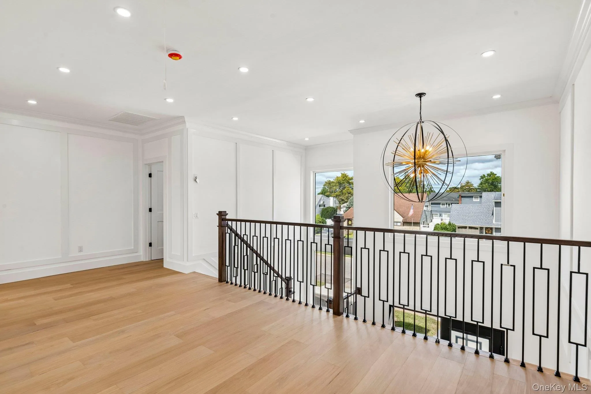 Hardwood flooring, contemporary chandelier, recessed lighting, white paneled walls, and dark metal stair railing with wood newel posts Hardwood flooring, contemporary chandelier, recessed lighting, white paneled walls, and dark metal stair railing with wood newel posts