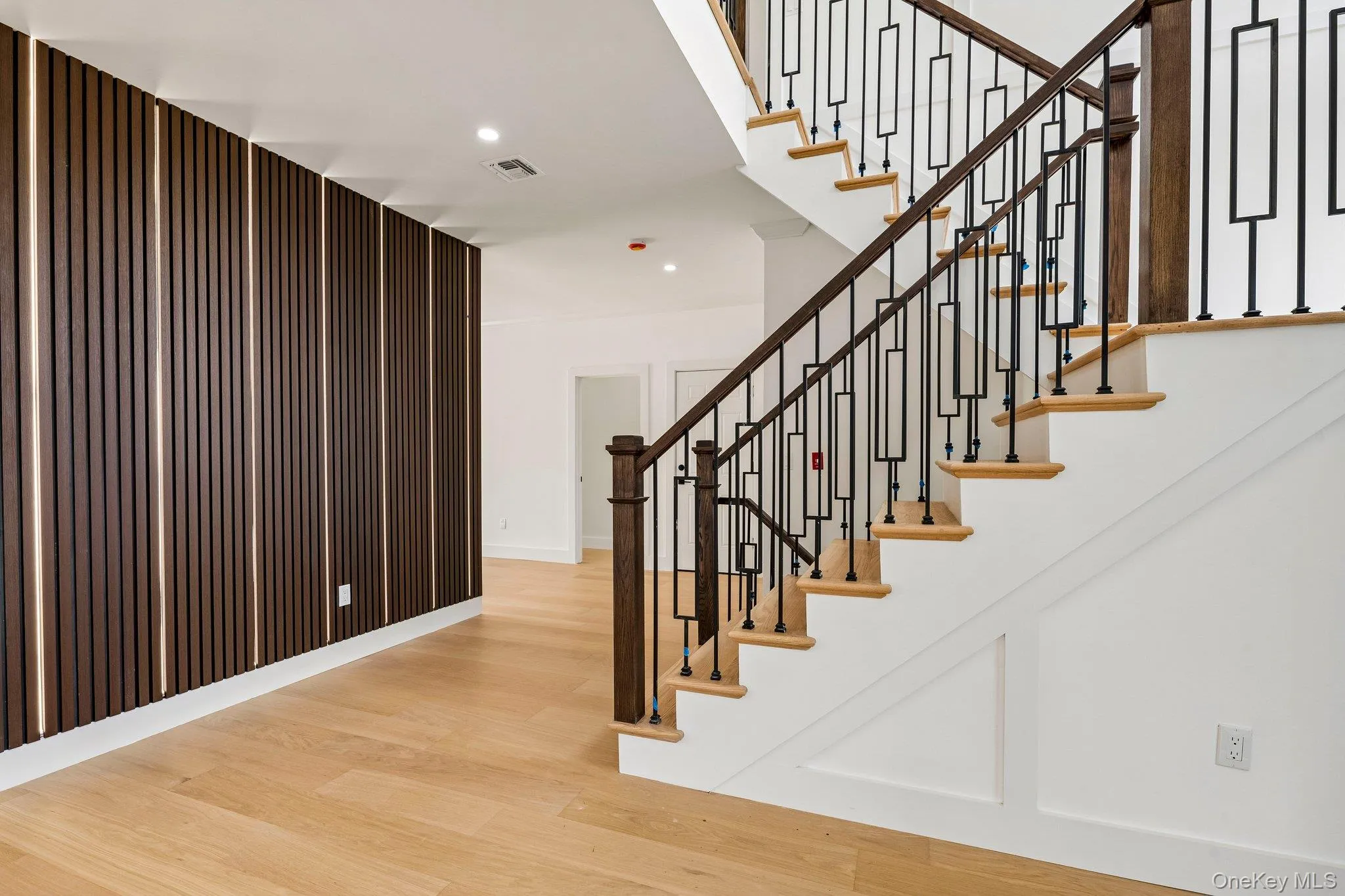 Hardwood flooring, custom wall paneling with integrated lighting, recessed ceiling lighting, staircase with decorative metal balusters, and a rich wood handrail Hardwood flooring, custom wall paneling with integrated lighting, recessed ceiling lighting, staircase with decorative metal balusters, and a rich wood handrail