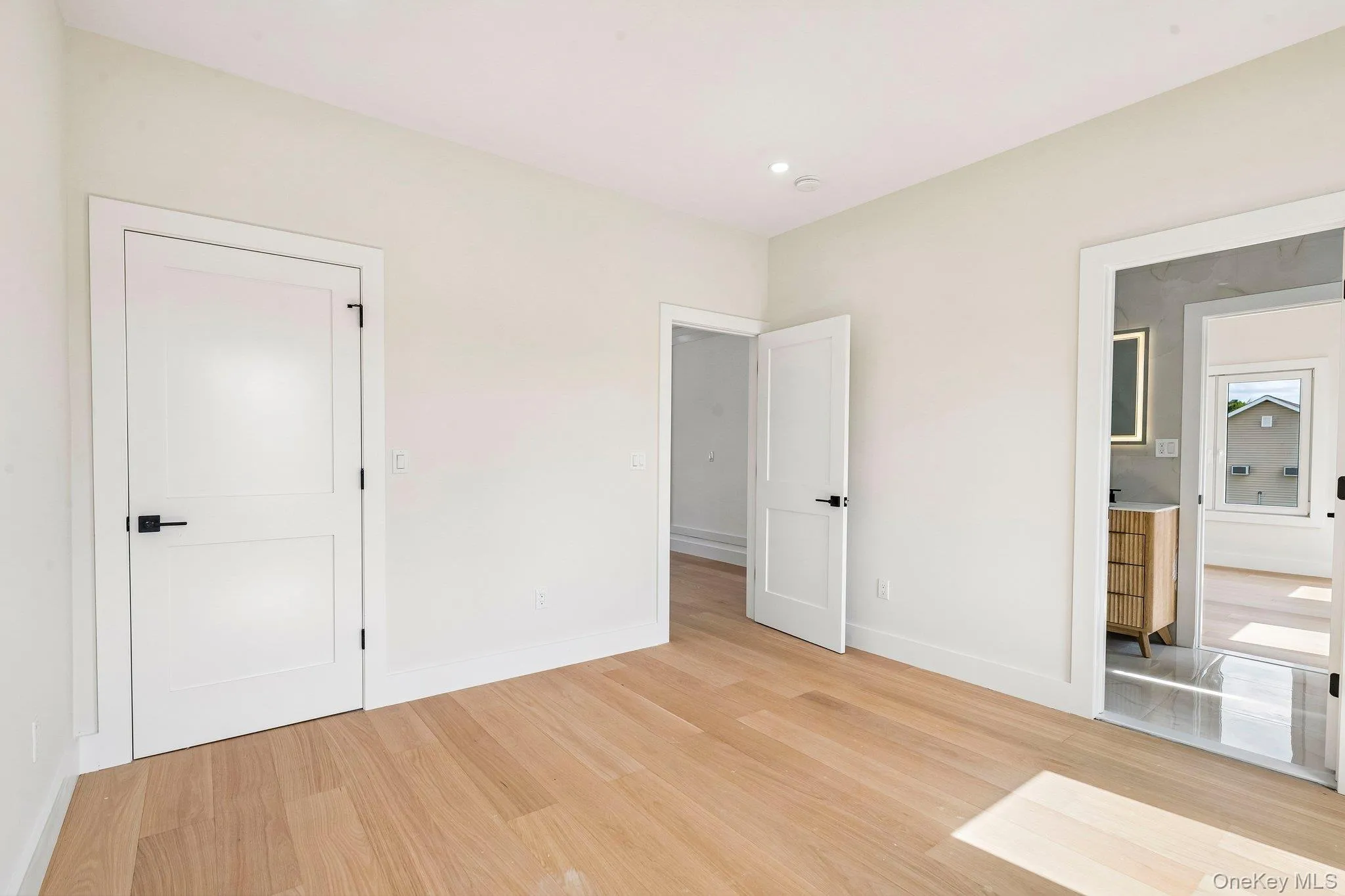 Light wood-finish flooring, recessed ceiling lighting, two-panel interior doors with black hardware, white baseboards Light wood-finish flooring, recessed ceiling lighting, two-panel interior doors with black hardware, white baseboards