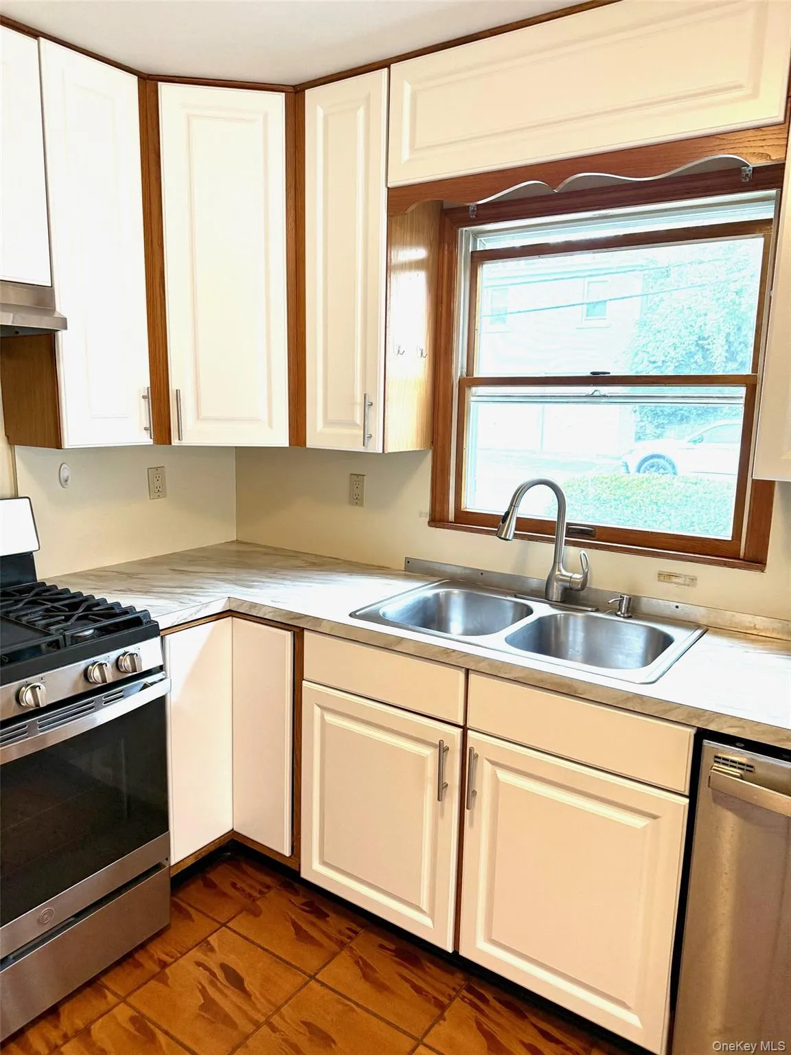 Kitchen featuring stainless steel appliances, white cabinets, light countertops, dark tile patterned floors, and under cabinet range hood Kitchen featuring stainless steel appliances, white cabinets, light countertops, dark tile patterned floors, and under cabinet range hood