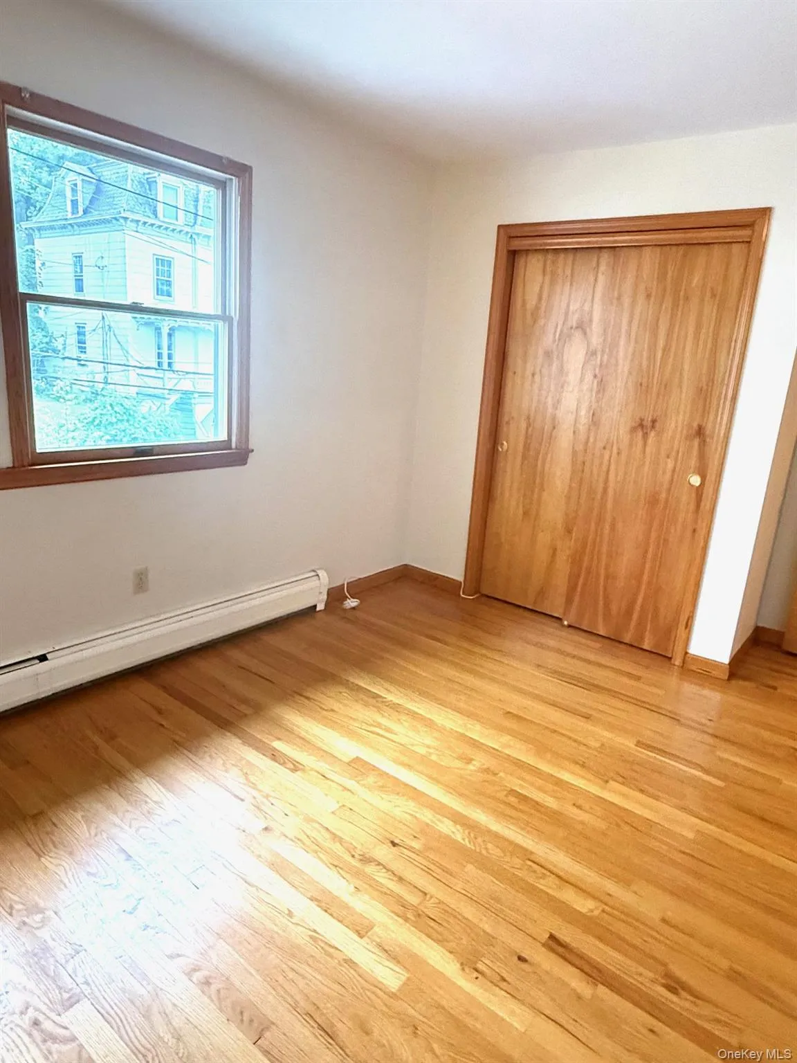 Unfurnished bedroom featuring a baseboard radiator, light wood-type flooring, and a closet Unfurnished bedroom featuring a baseboard radiator, light wood-type flooring, and a closet