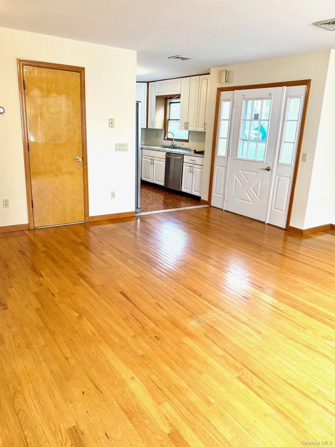 Kitchen featuring light wood finished floors, stainless steel dishwasher, white cabinets, open floor plan, and light countertops Kitchen featuring light wood finished floors, stainless steel dishwasher, white cabinets, open floor plan, and light countertops