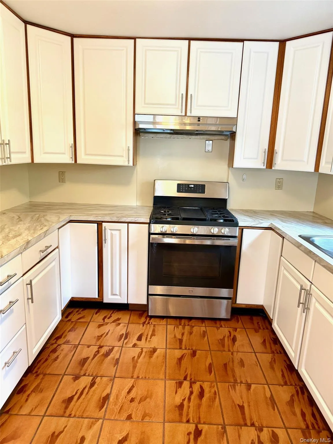 Kitchen with stainless steel gas range, white cabinets, light tile patterned floors, and light countertops Kitchen with stainless steel gas range, white cabinets, light tile patterned floors, and light countertops