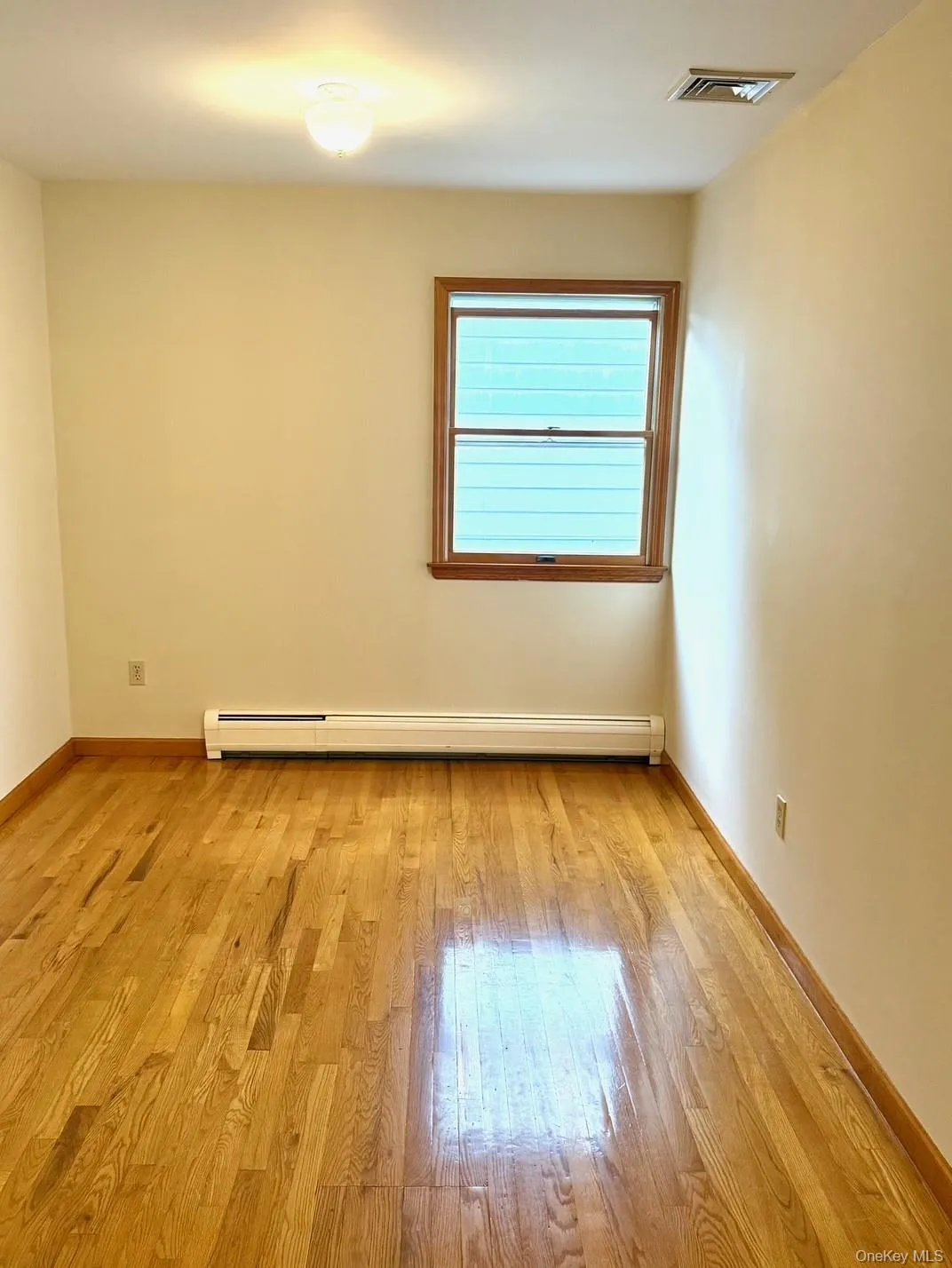 Empty room featuring light wood-style flooring and a baseboard heating unit Empty room featuring light wood-style flooring and a baseboard heating unit