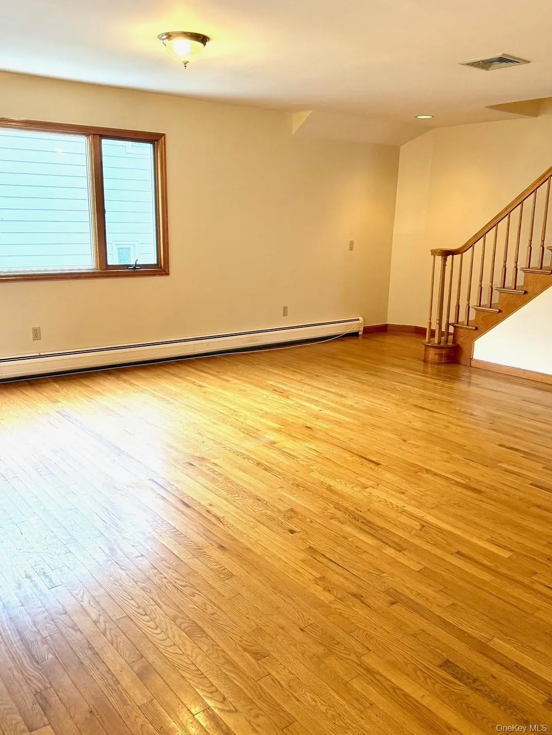 Empty room with light wood-style flooring, stairway, and a baseboard radiator Empty room with light wood-style flooring, stairway, and a baseboard radiator