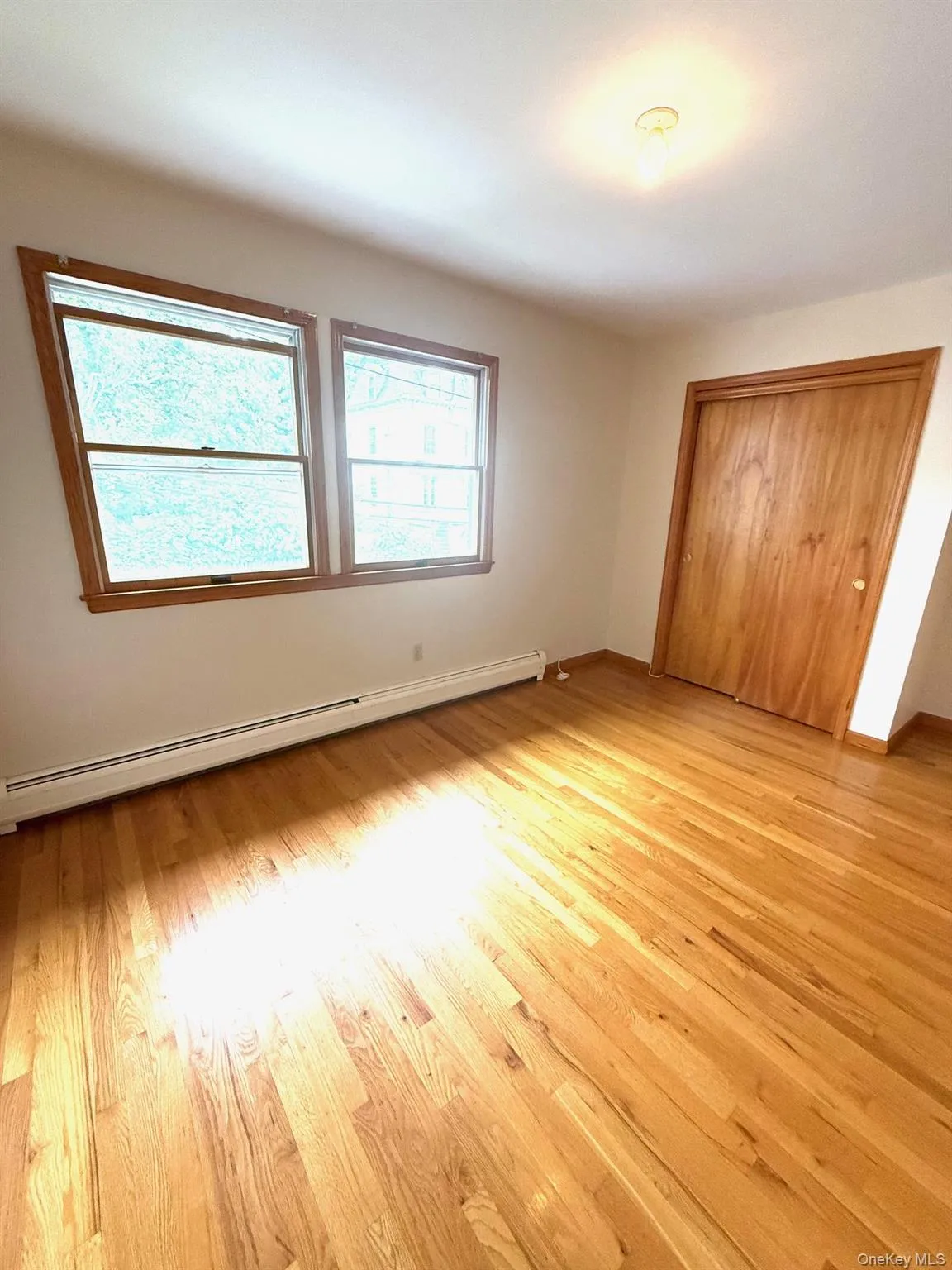 Unfurnished bedroom with a baseboard radiator, light wood-style flooring, and a closet Unfurnished bedroom with a baseboard radiator, light wood-style flooring, and a closet