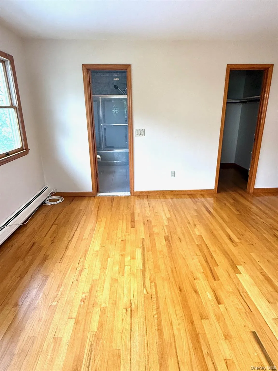 Primary bedroom/Primary bath and walk-in closet, baseboard heating unit, light wood-style floors, and a spacious closet Primary bedroom/Primary bath and walk-in closet, baseboard heating unit, light wood-style floors, and a spacious closet