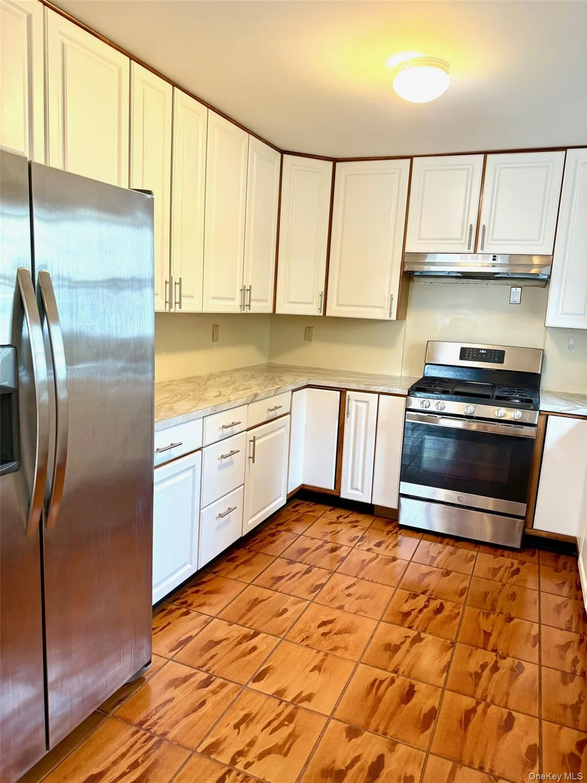 Kitchen featuring appliances with stainless steel finishes, white cabinetry, light tile patterned floors, and under cabinet range hood Kitchen featuring appliances with stainless steel finishes, white cabinetry, light tile patterned floors, and under cabinet range hood