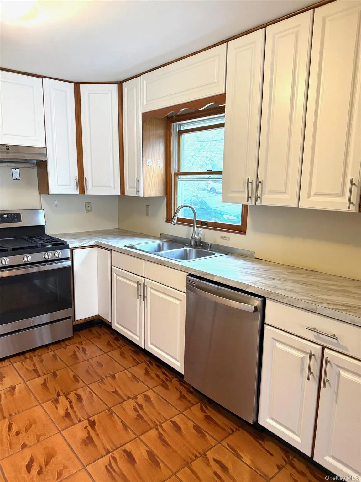Kitchen featuring white cabinets, stainless steel appliances, light countertops, and dark tile patterned floors Kitchen featuring white cabinets, stainless steel appliances, light countertops, and dark tile patterned floors