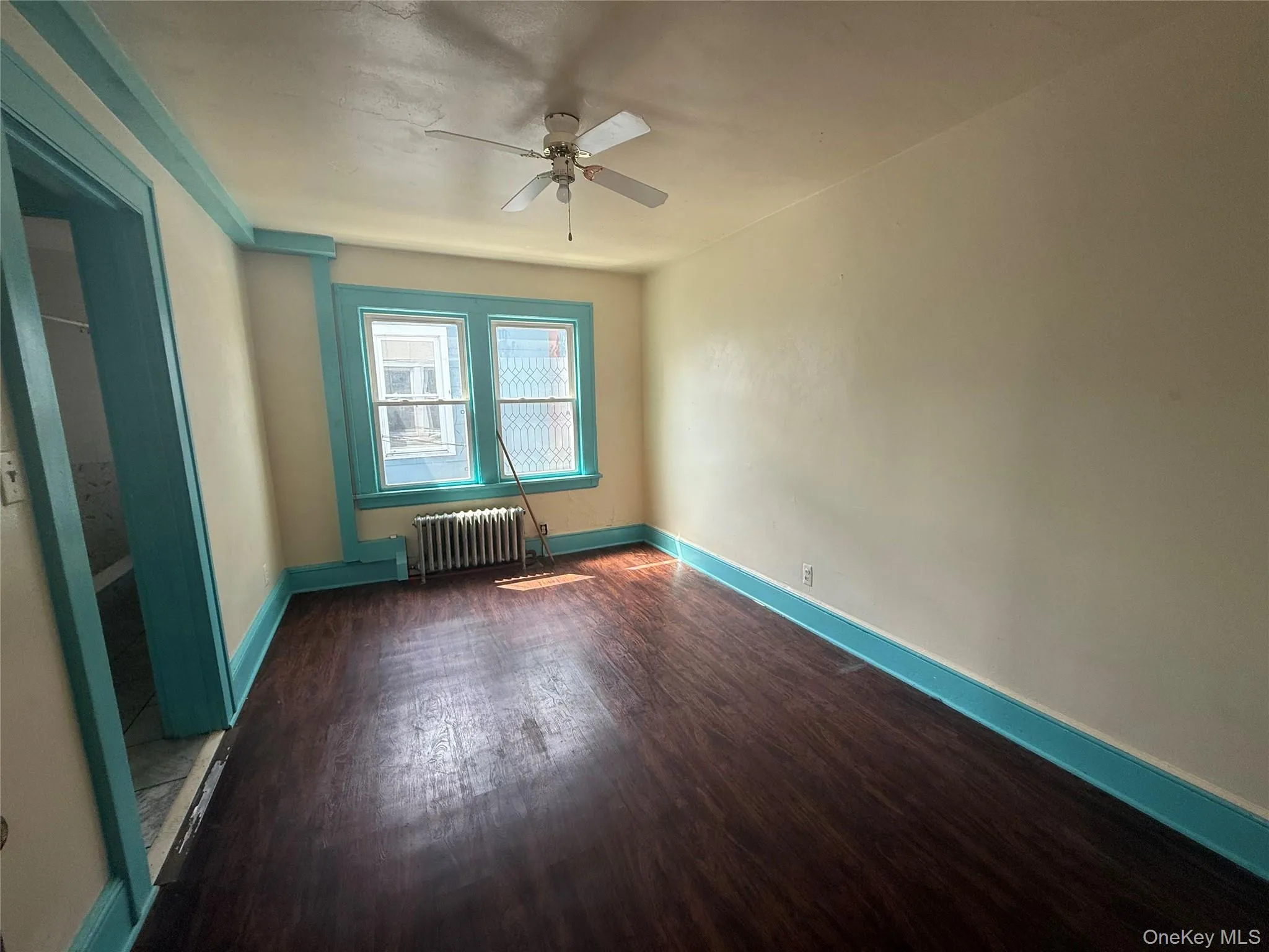 Empty room with dark wood-style flooring, radiator, and ceiling fan Empty room with dark wood-style flooring, radiator, and ceiling fan