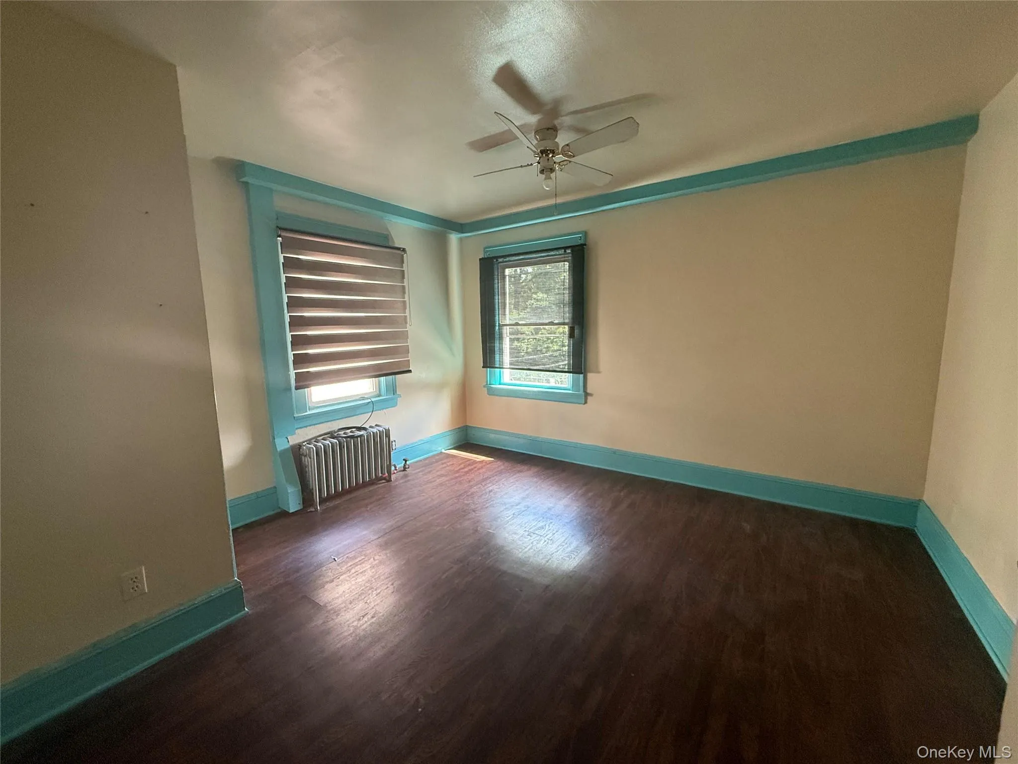 Empty room featuring dark wood-style floors, radiator heating unit, and ceiling fan Empty room featuring dark wood-style floors, radiator heating unit, and ceiling fan