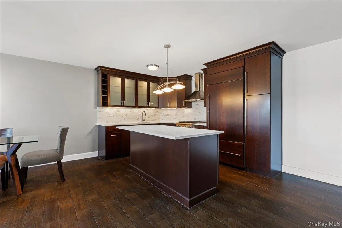 Kitchen with an island, lighted glass insert cabinets, backsplash, decorative light fixtures, and dark brown cabinets Kitchen with an island, lighted glass insert cabinets, backsplash, decorative light fixtures, and dark brown cabinets