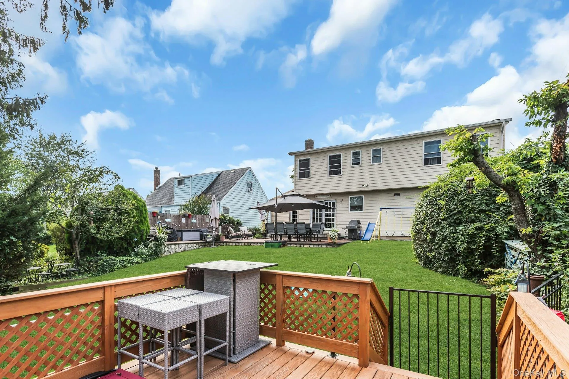 Wood-finish deck with lattice railing, private green lawn, mature perimeter landscaping, and a back patio Wood-finish deck with lattice railing, private green lawn, mature perimeter landscaping, and a back patio