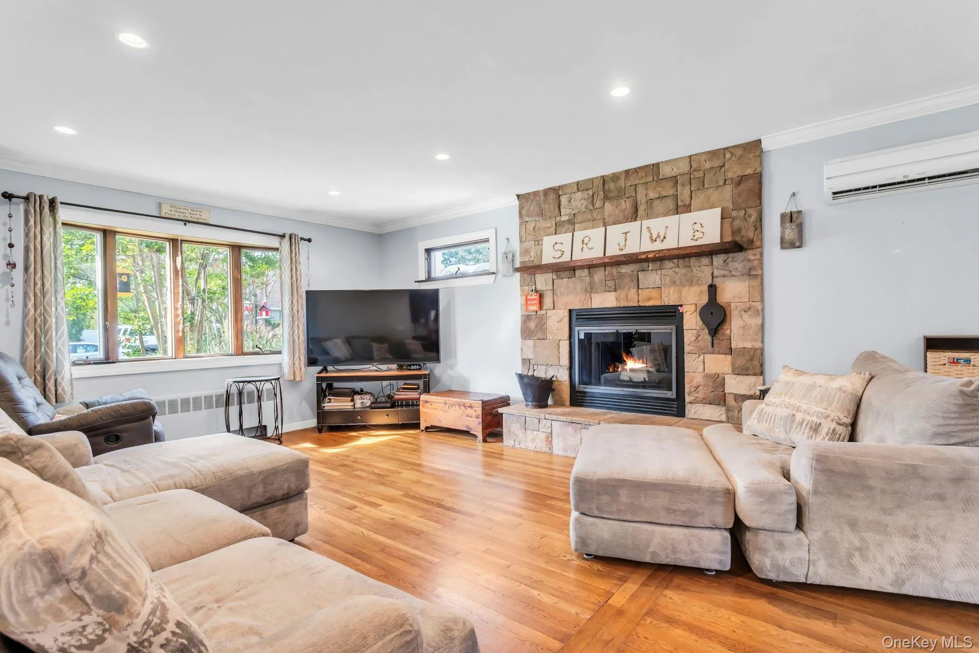 Hardwood flooring throughout, stone-clad fireplace with hearth and wood mantel, large multi-pane window, recessed lighting, and crown molding Hardwood flooring throughout, stone-clad fireplace with hearth and wood mantel, large multi-pane window, recessed lighting, and crown molding