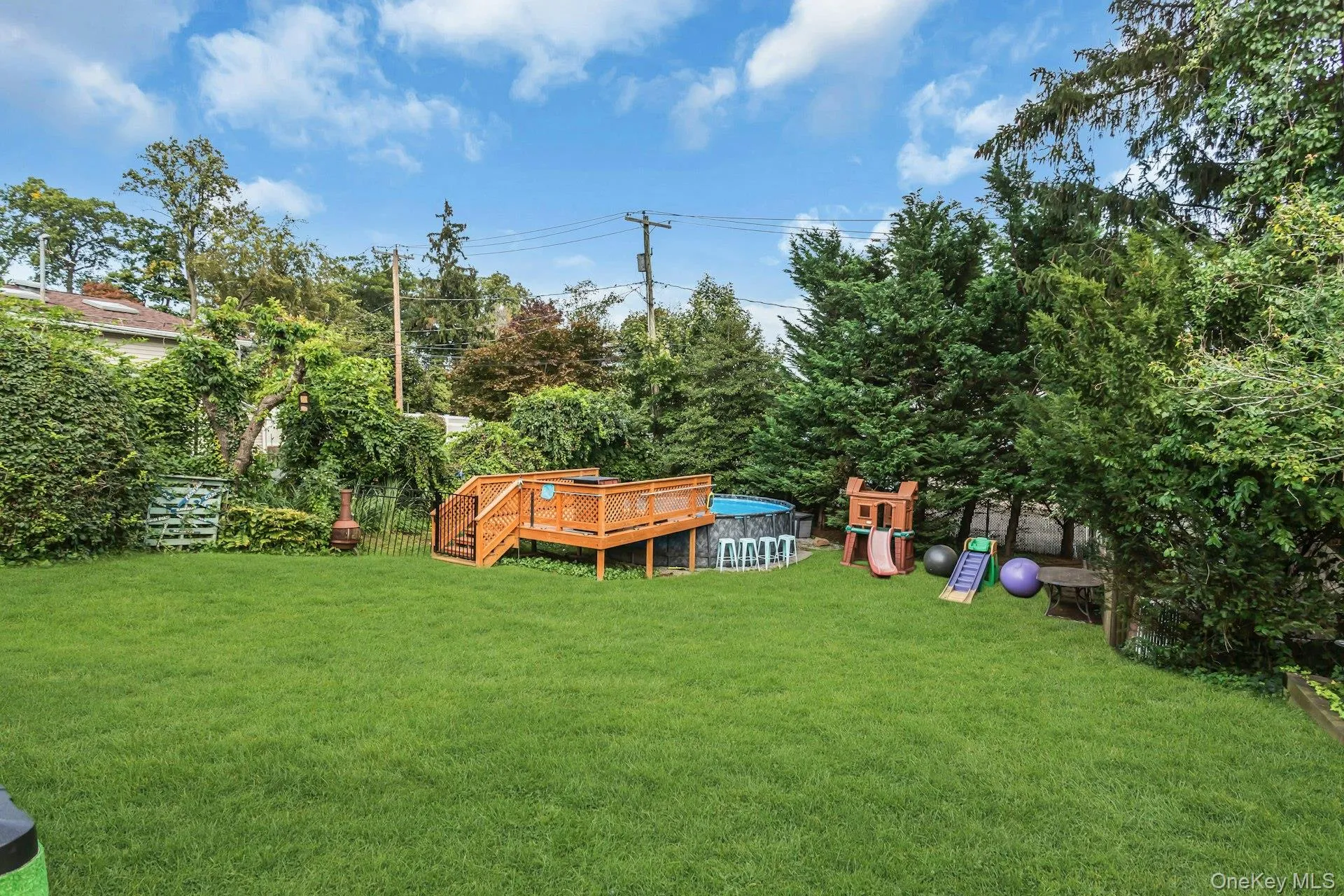 Expansive green lawn featuring a wooden deck, an above-ground pool, and mature perimeter trees Expansive green lawn featuring a wooden deck, an above-ground pool, and mature perimeter trees