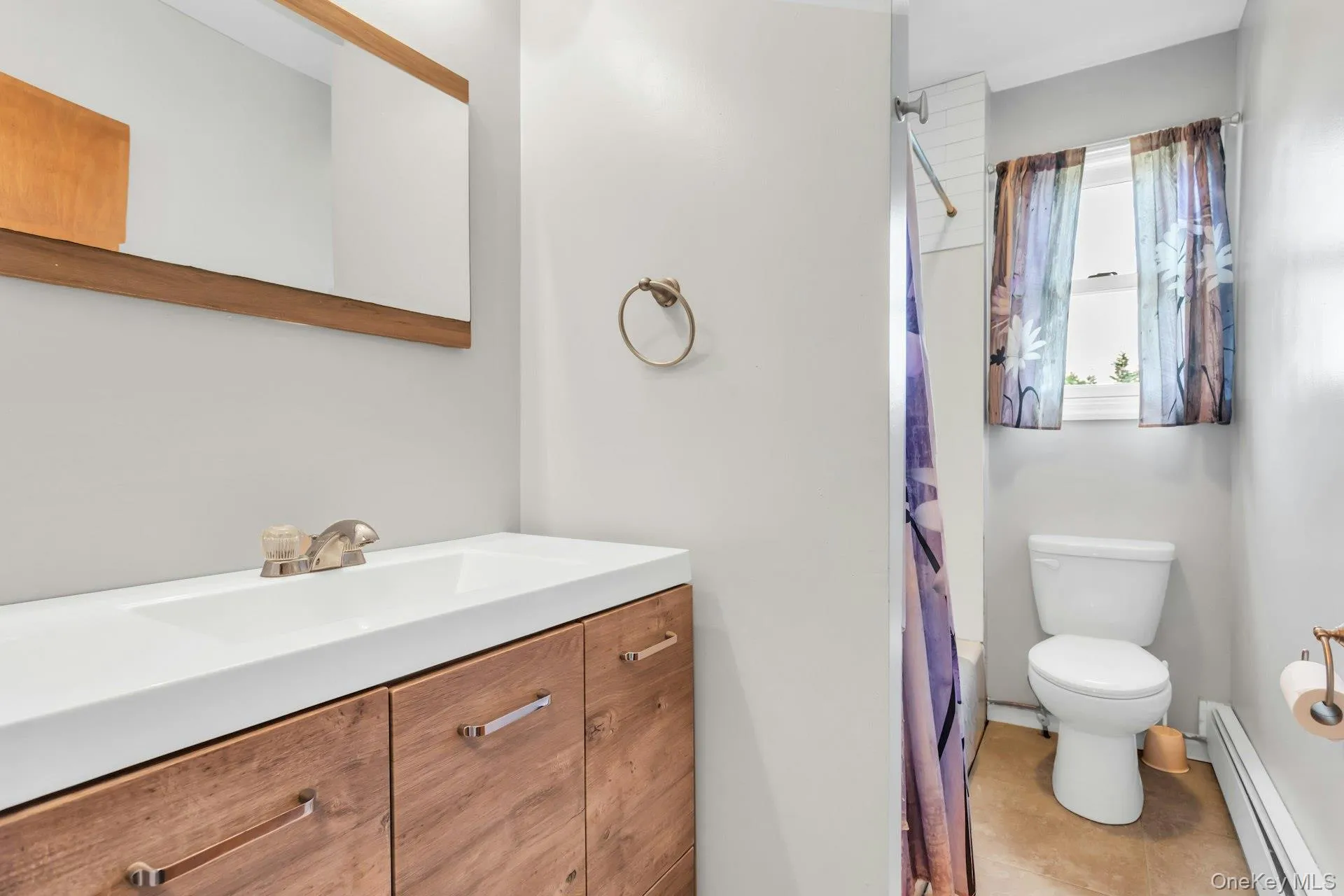 Bathroom featuring a wood-finish vanity with an integrated sink, a framed mirror, and a window with a white frame Bathroom featuring a wood-finish vanity with an integrated sink, a framed mirror, and a window with a white frame