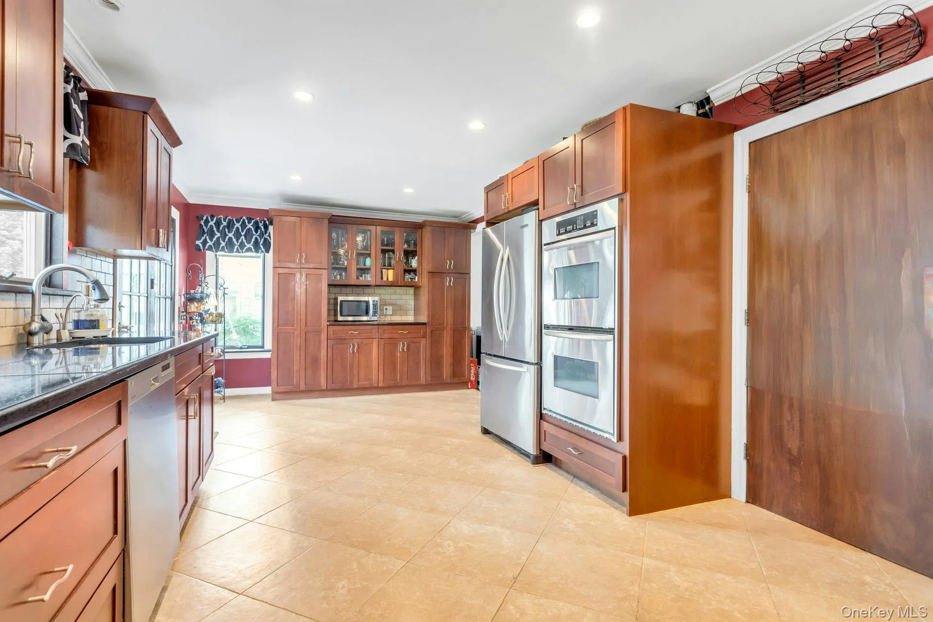 Full kitchen with extensive wood cabinetry, stainless steel appliances, dark countertops, tile flooring, and recessed lighting Full kitchen with extensive wood cabinetry, stainless steel appliances, dark countertops, tile flooring, and recessed lighting