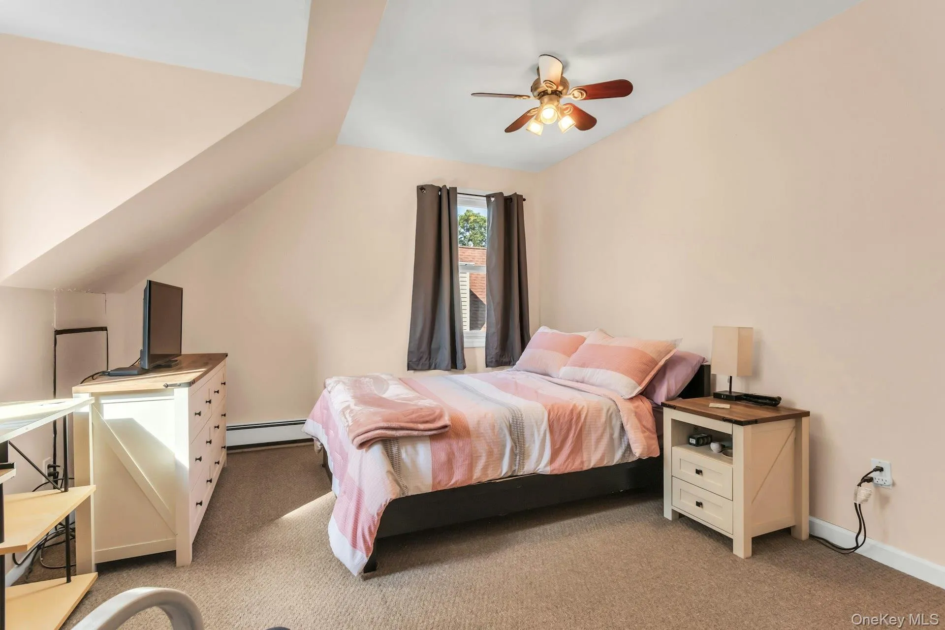 Sloped ceiling room featuring a ceiling fan, carpeted flooring, and a single window with curtains Sloped ceiling room featuring a ceiling fan, carpeted flooring, and a single window with curtains