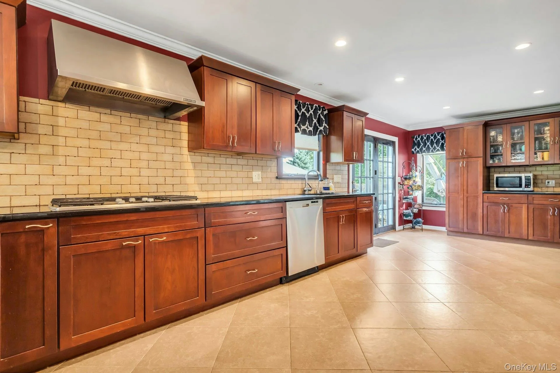 Kitchen featuring wood cabinetry, stainless steel range hood, tile backsplash, black countertops, and recessed lighting Kitchen featuring wood cabinetry, stainless steel range hood, tile backsplash, black countertops, and recessed lighting