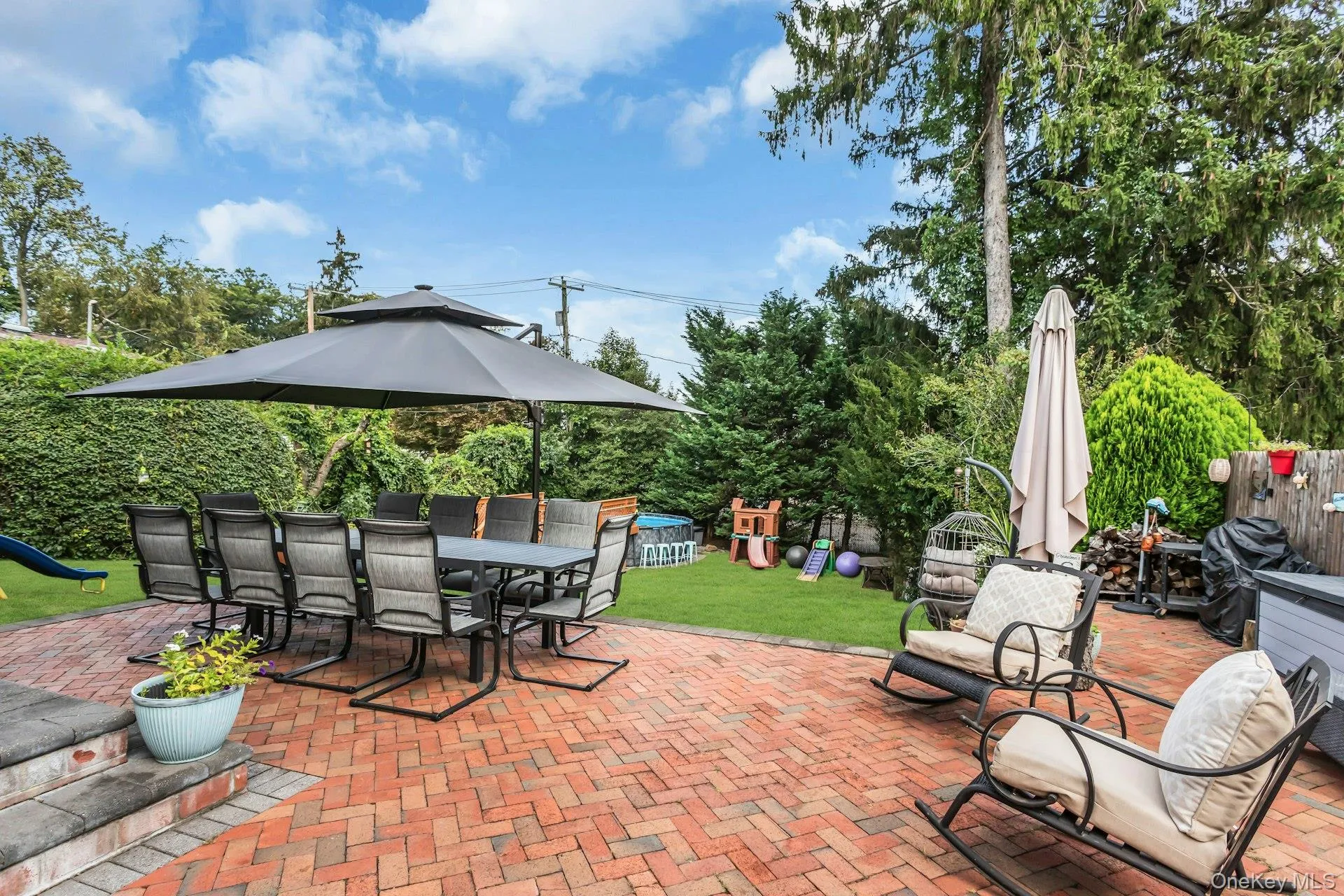 Expansive backyard featuring a red brick patio, a manicured lawn, and mature perimeter trees Expansive backyard featuring a red brick patio, a manicured lawn, and mature perimeter trees