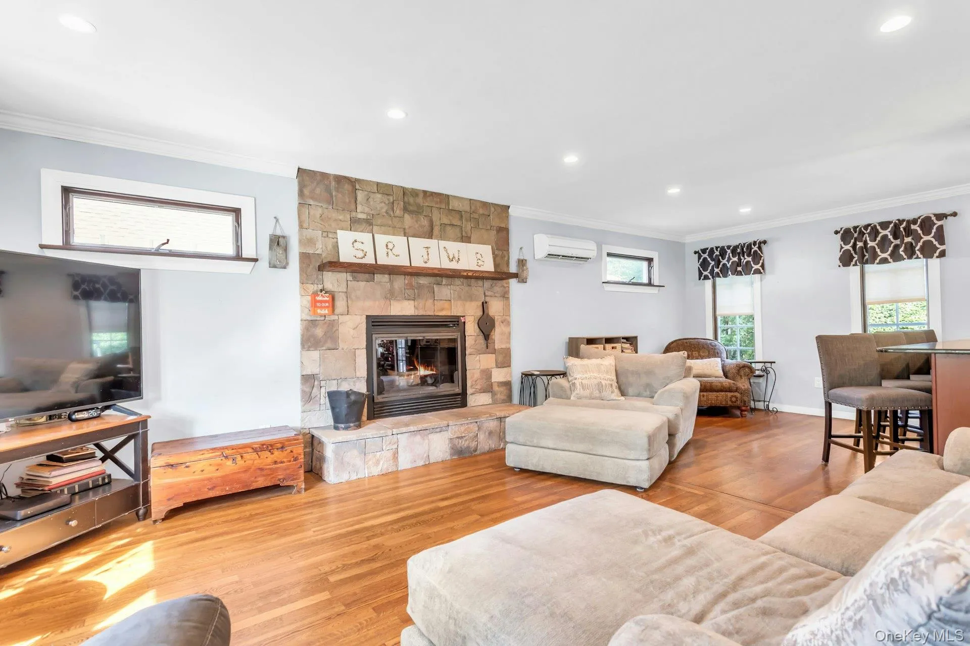 Stone-surround fireplace with hearth, wood-finish flooring, recessed lighting, crown molding, and clerestory windows Stone-surround fireplace with hearth, wood-finish flooring, recessed lighting, crown molding, and clerestory windows