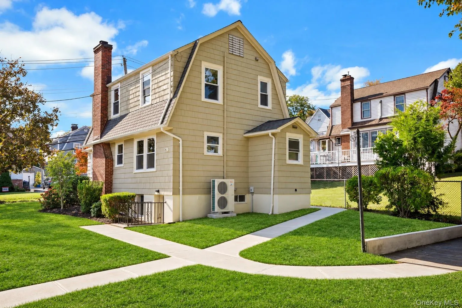 Gambrel-roof exterior featuring shingle siding, a brick chimney, and concrete walkways set within a manicured lawn Gambrel-roof exterior featuring shingle siding, a brick chimney, and concrete walkways set within a manicured lawn