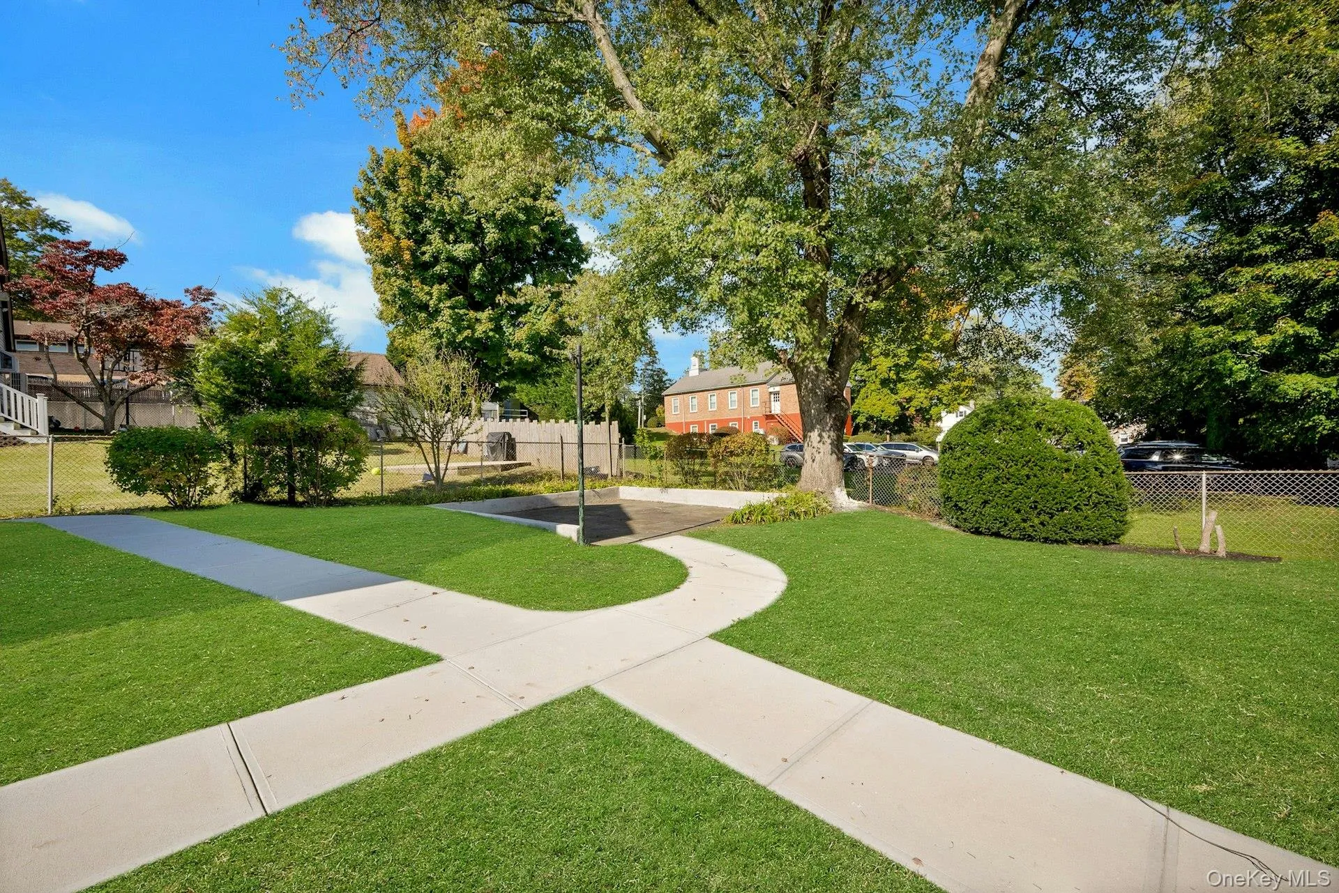 Spacious lawn area featuring concrete pathways, established trees, and perimeter fencing Spacious lawn area featuring concrete pathways, established trees, and perimeter fencing