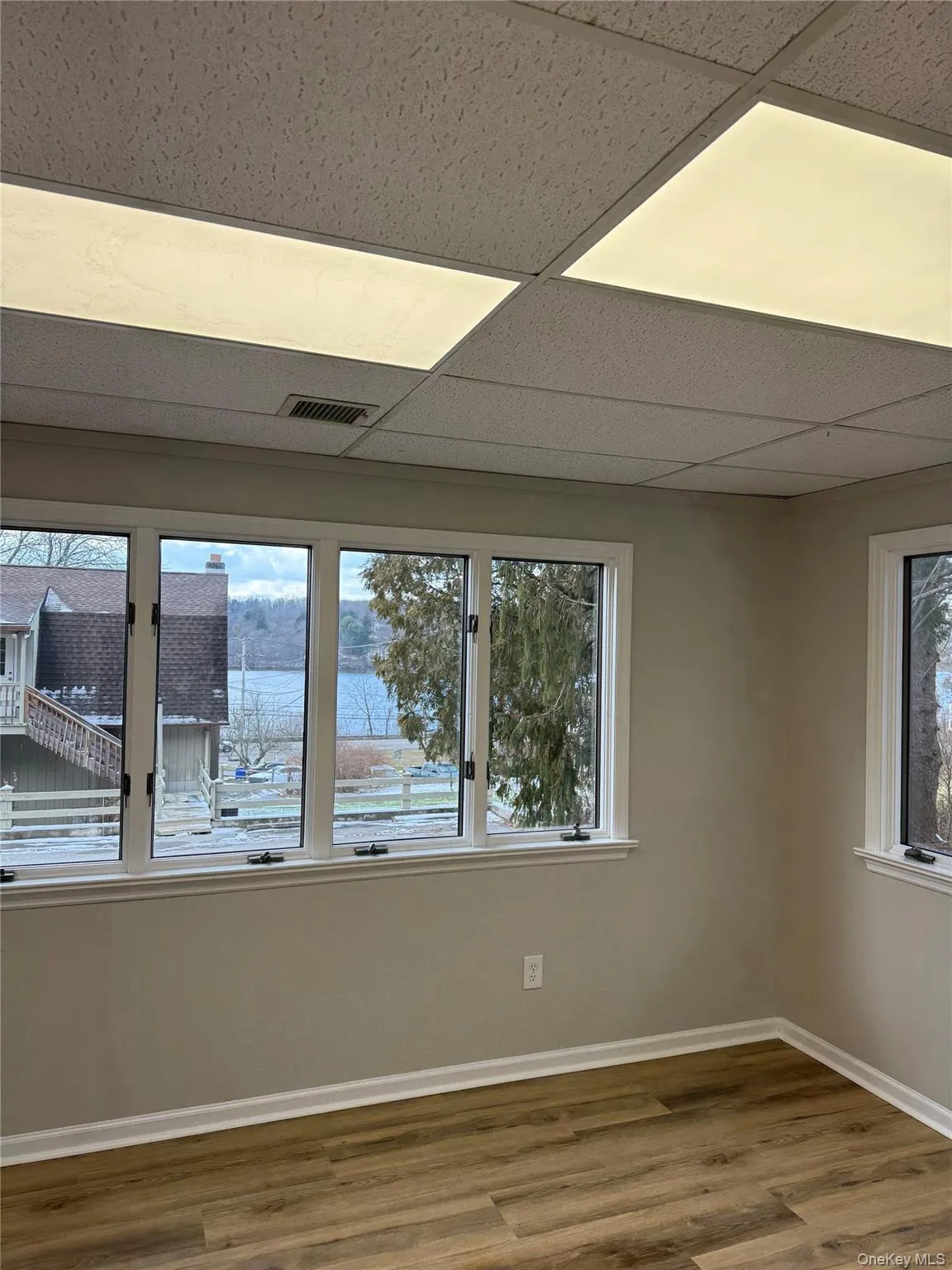 Empty room featuring plenty of natural light, a paneled ceiling, and wood finished floors Empty room featuring plenty of natural light, a paneled ceiling, and wood finished floors