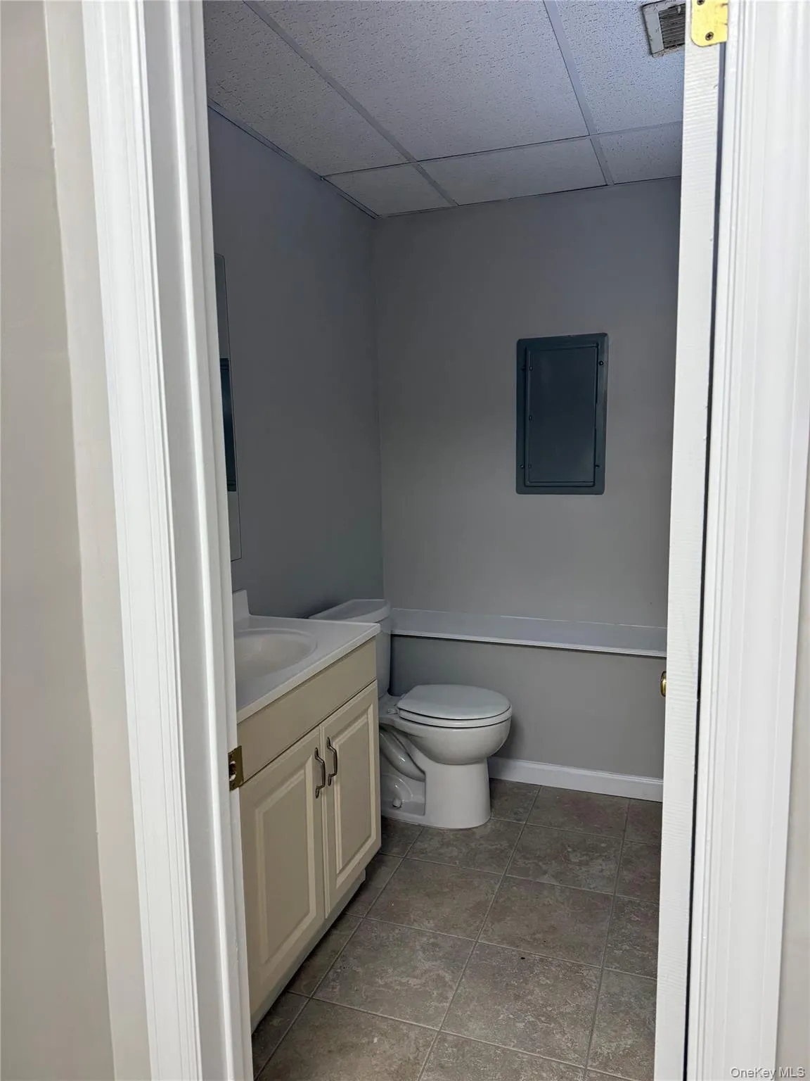 Full bathroom with vanity, a paneled ceiling, electric panel, and light tile patterned floors Full bathroom with vanity, a paneled ceiling, electric panel, and light tile patterned floors