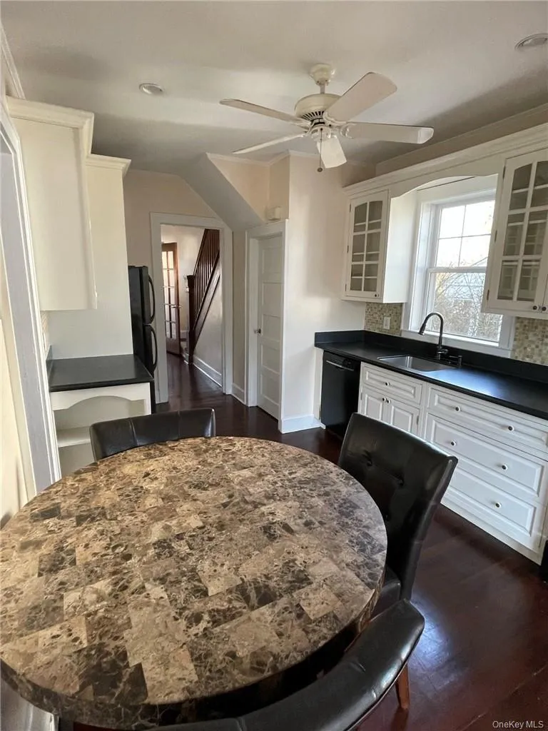 Kitchen featuring white cabinets, black appliances, dark hardwood floors, fan and kitchen table. Kitchen featuring white cabinets, black appliances, dark hardwood floors, fan and kitchen table.