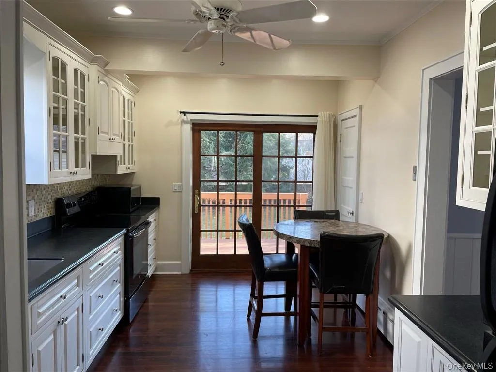 Kitchen featuring white cabinets, black appliances, dark hardwood floors, sliding doors to access rear deck and back yard and a kitchen table Kitchen featuring white cabinets, black appliances, dark hardwood floors, sliding doors to access rear deck and back yard and a kitchen table