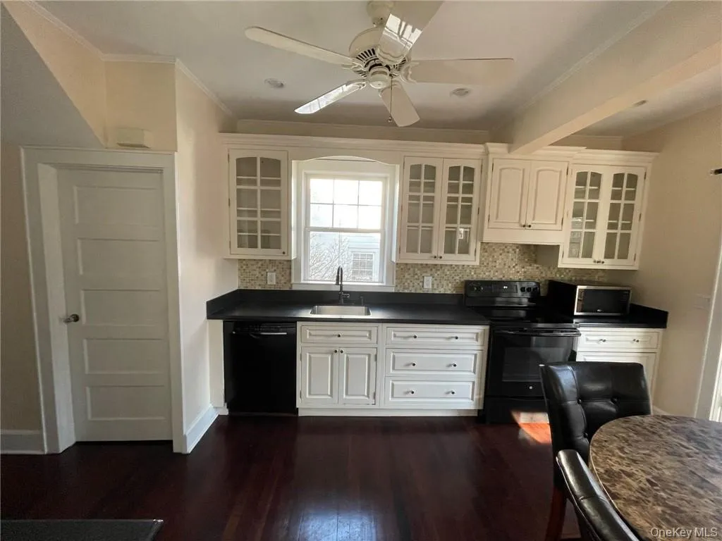 Kitchen featuring white cabinets, black appliances, dark hardwood floors and fan. Kitchen featuring white cabinets, black appliances, dark hardwood floors and fan.