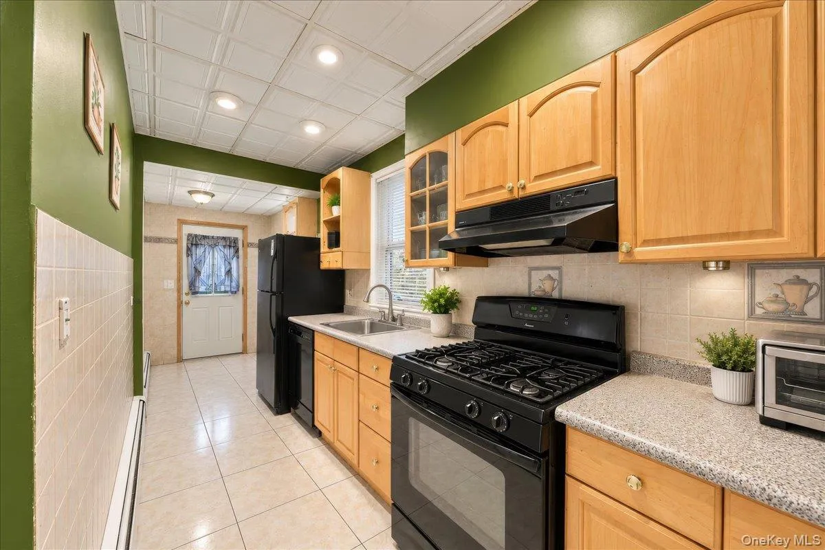 Wood-finish cabinetry, black appliances, speckled countertops, tile flooring, and a tiled backsplash Wood-finish cabinetry, black appliances, speckled countertops, tile flooring, and a tiled backsplash