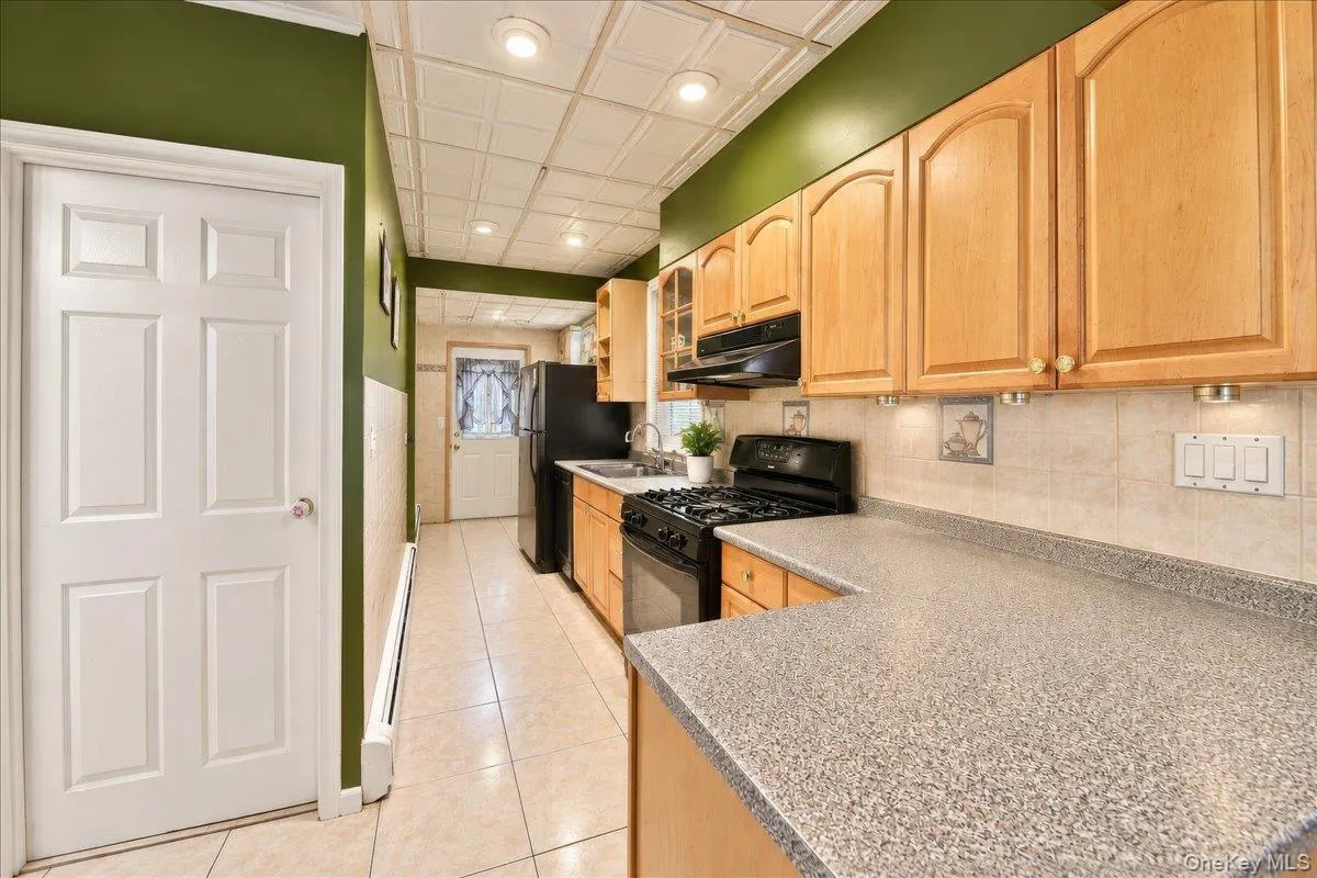 Galley kitchen featuring natural wood cabinetry, speckled quartz countertops, stainless steel appliances, and tile flooring Galley kitchen featuring natural wood cabinetry, speckled quartz countertops, stainless steel appliances, and tile flooring
