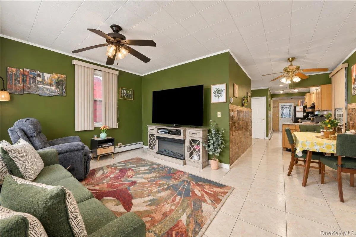 Living area featuring tile flooring, ceiling fans with integrated lighting, window with vertical blinds, and a built-in electric fireplace Living area featuring tile flooring, ceiling fans with integrated lighting, window with vertical blinds, and a built-in electric fireplace