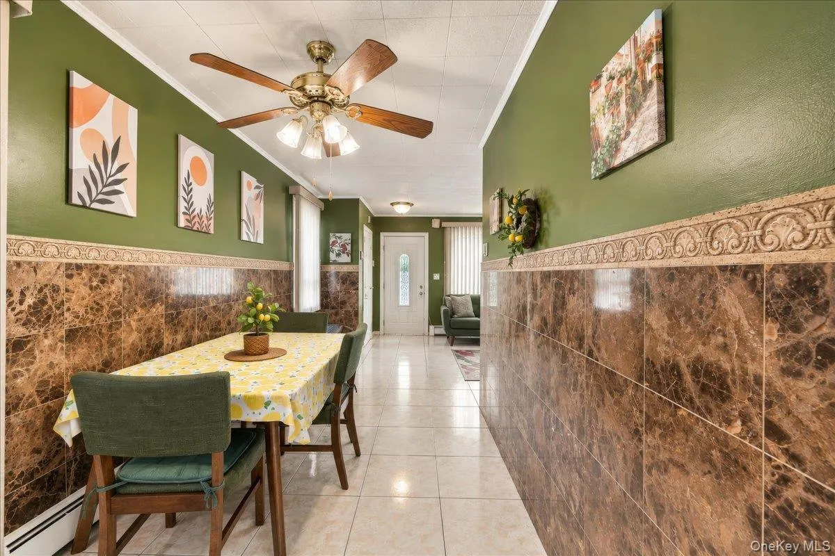 Full-height wall paneling with decorative trim, wood-finish ceiling fan with integrated lighting, and tile flooring Full-height wall paneling with decorative trim, wood-finish ceiling fan with integrated lighting, and tile flooring