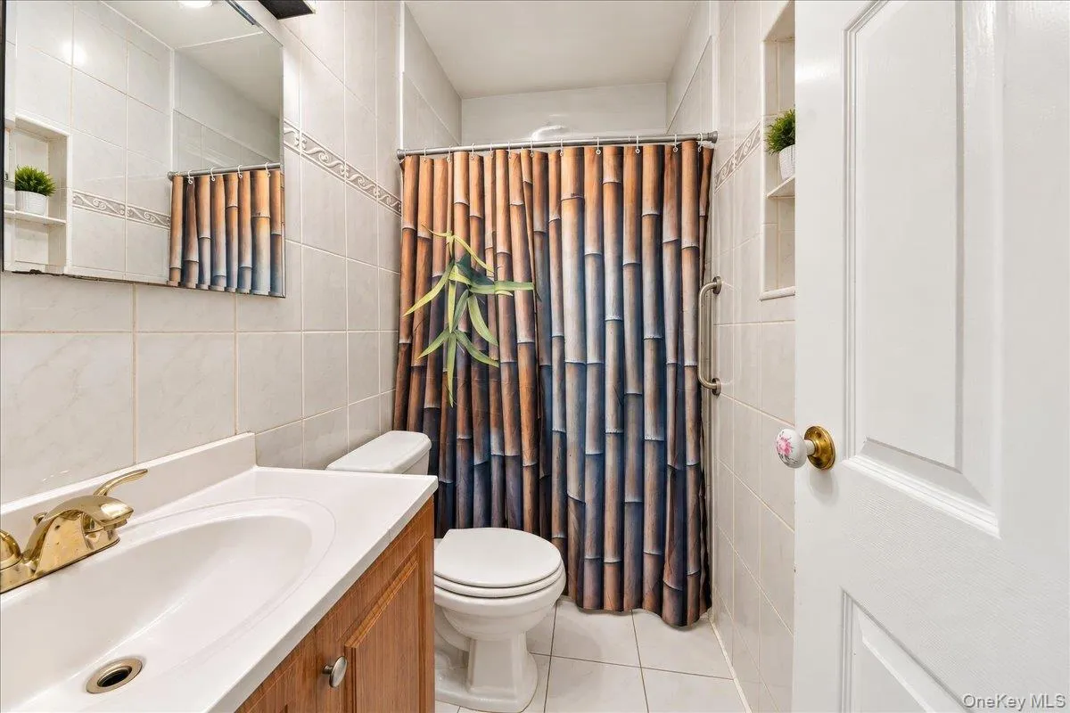 Bathroom featuring a vanity with an integrated sink, a toilet, a shower area with a grab bar, and recessed shelving Bathroom featuring a vanity with an integrated sink, a toilet, a shower area with a grab bar, and recessed shelving