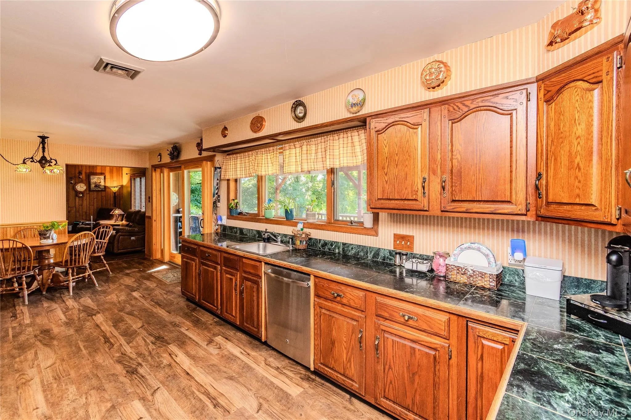 Wood-finish flooring throughout, solid wood cabinetry, dark countertops, stainless steel dishwasher, and sliding glass door Wood-finish flooring throughout, solid wood cabinetry, dark countertops, stainless steel dishwasher, and sliding glass door