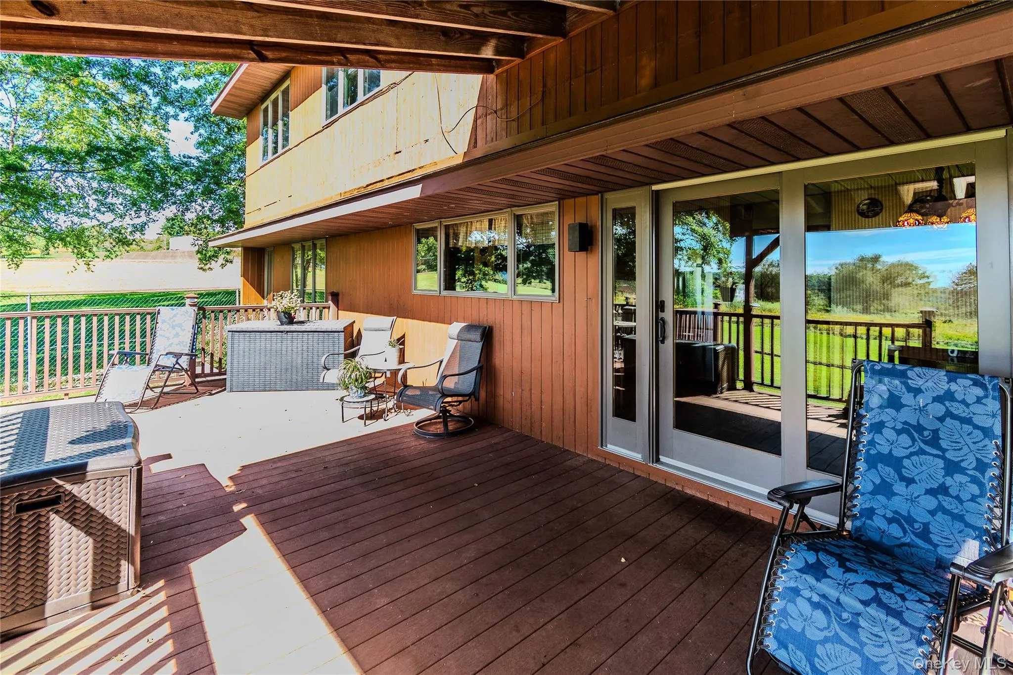 Expansive outdoor deck with wood-finish flooring, sliding glass doors, and a wood-paneled exterior Expansive outdoor deck with wood-finish flooring, sliding glass doors, and a wood-paneled exterior