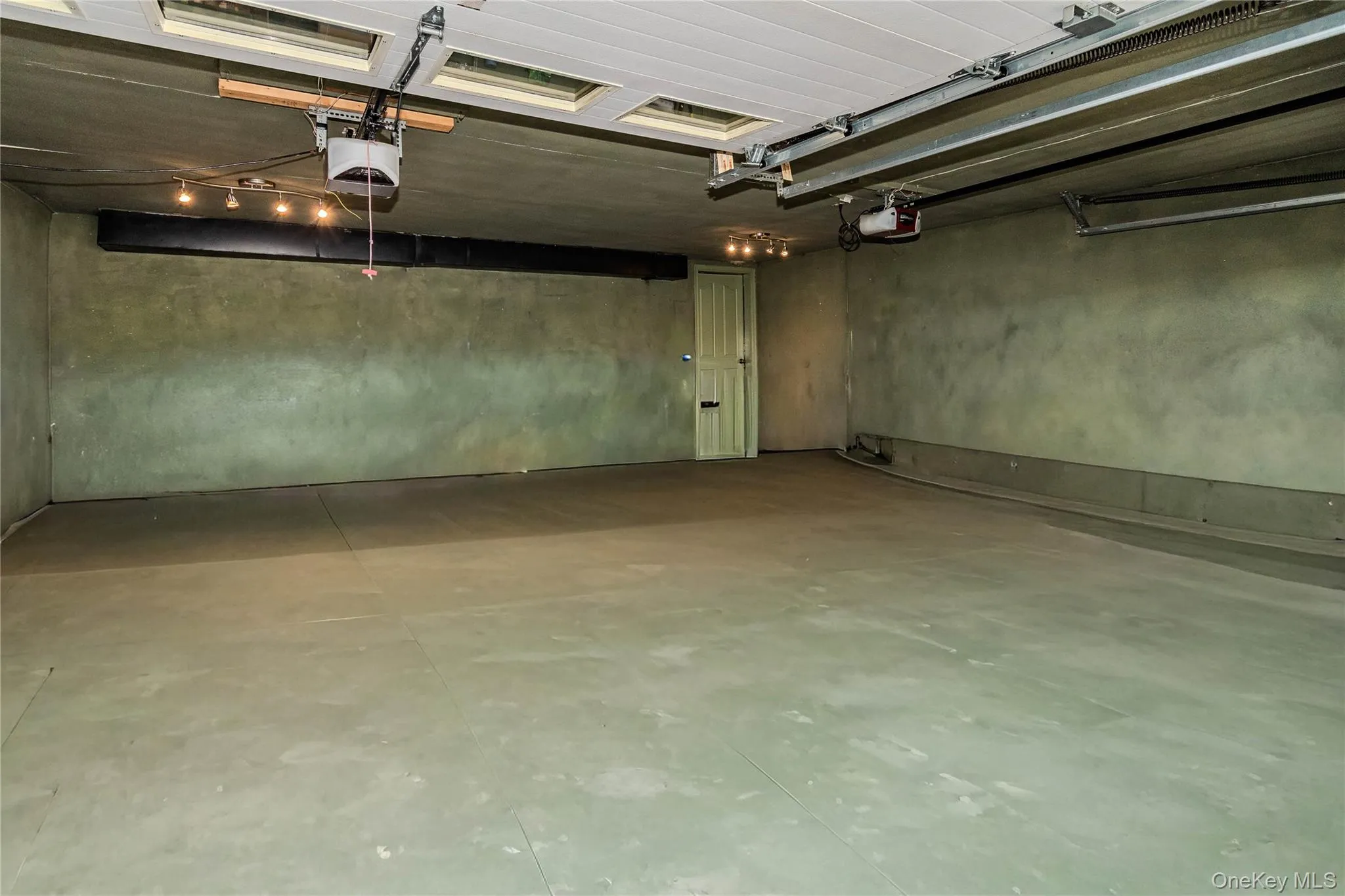 Expansive garage space with concrete flooring, overhead lighting, and two garage door openers Expansive garage space with concrete flooring, overhead lighting, and two garage door openers