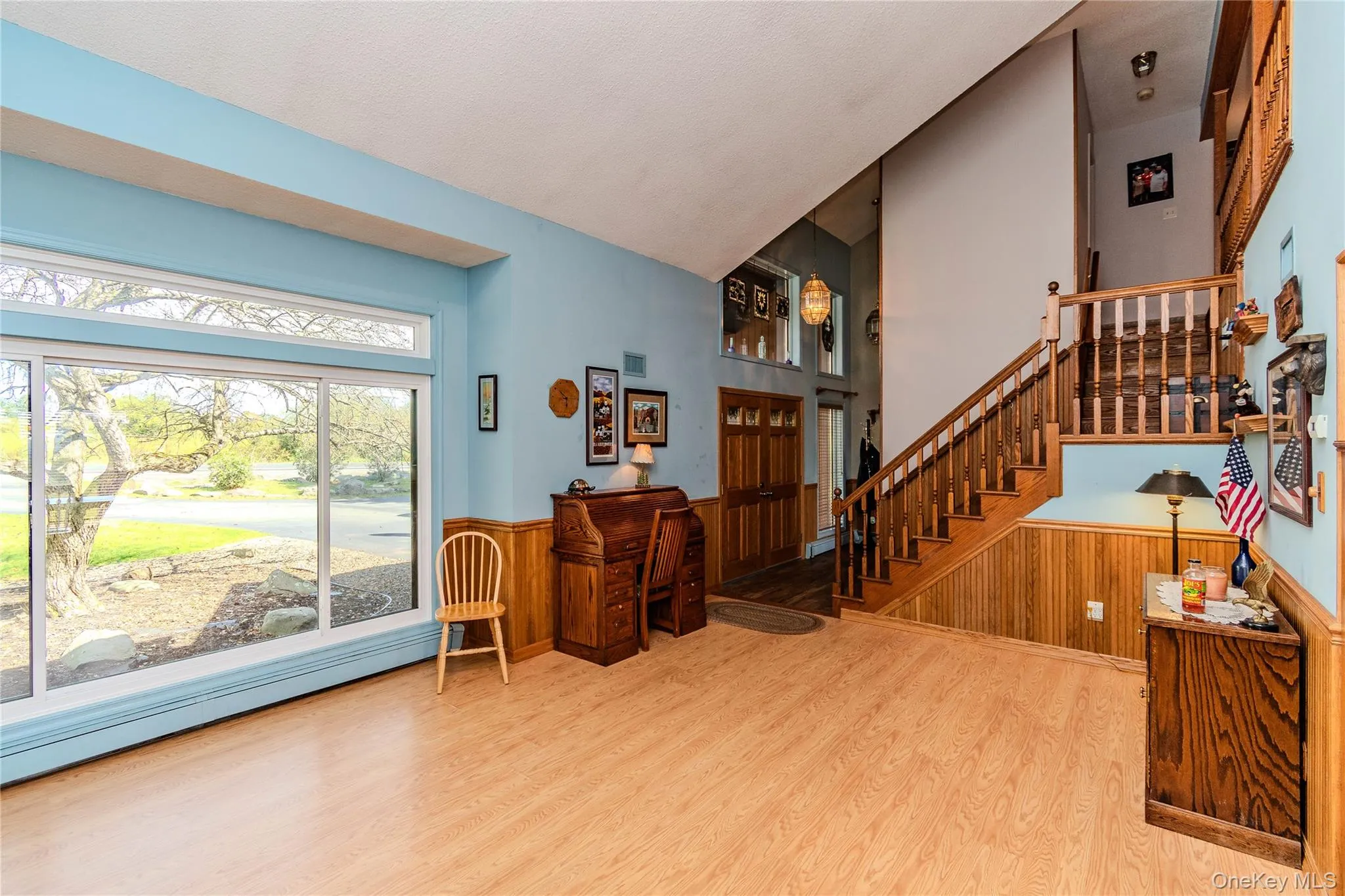 Expansive front window, wood-finish flooring, wood paneling, and a wood staircase with balusters Expansive front window, wood-finish flooring, wood paneling, and a wood staircase with balusters