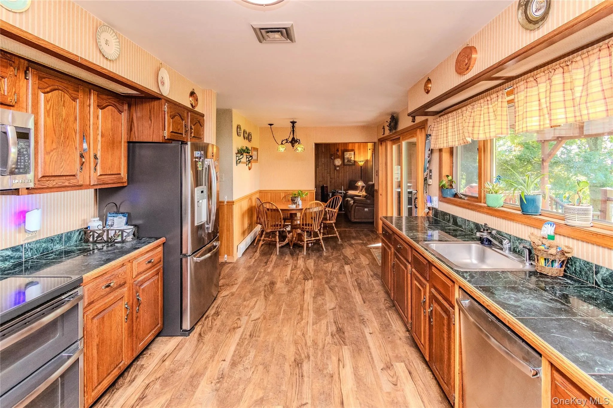 Kitchen featuring wood-finish flooring, wood cabinetry, dark countertops, and stainless steel appliances Kitchen featuring wood-finish flooring, wood cabinetry, dark countertops, and stainless steel appliances