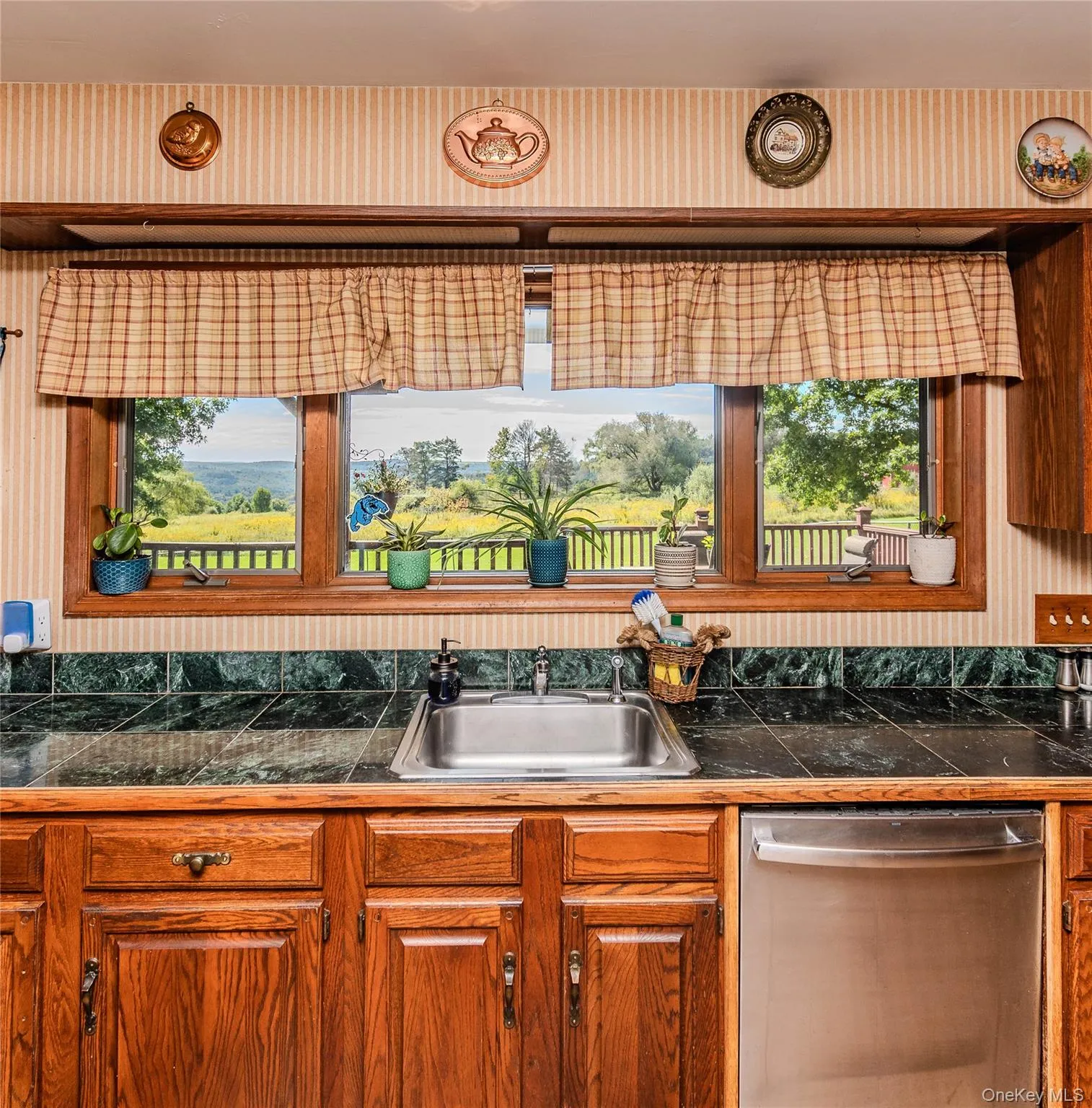 Wood-finish cabinetry, stainless steel sink, tile backsplash, and wood-framed windows Wood-finish cabinetry, stainless steel sink, tile backsplash, and wood-framed windows
