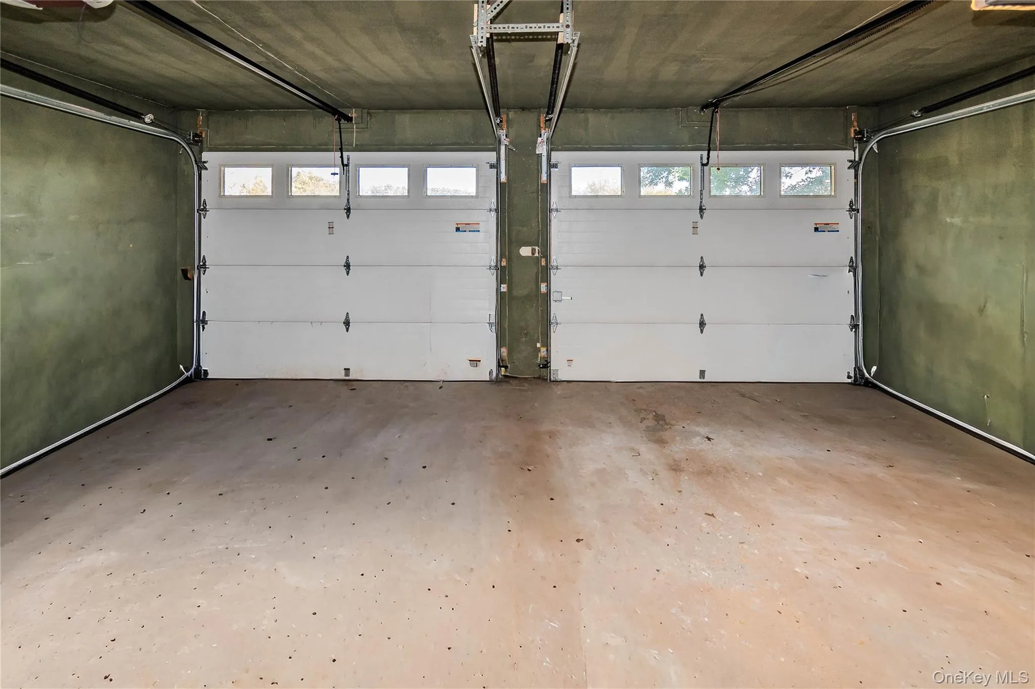 Two-car garage featuring concrete flooring and two white overhead doors with individual window panels Two-car garage featuring concrete flooring and two white overhead doors with individual window panels