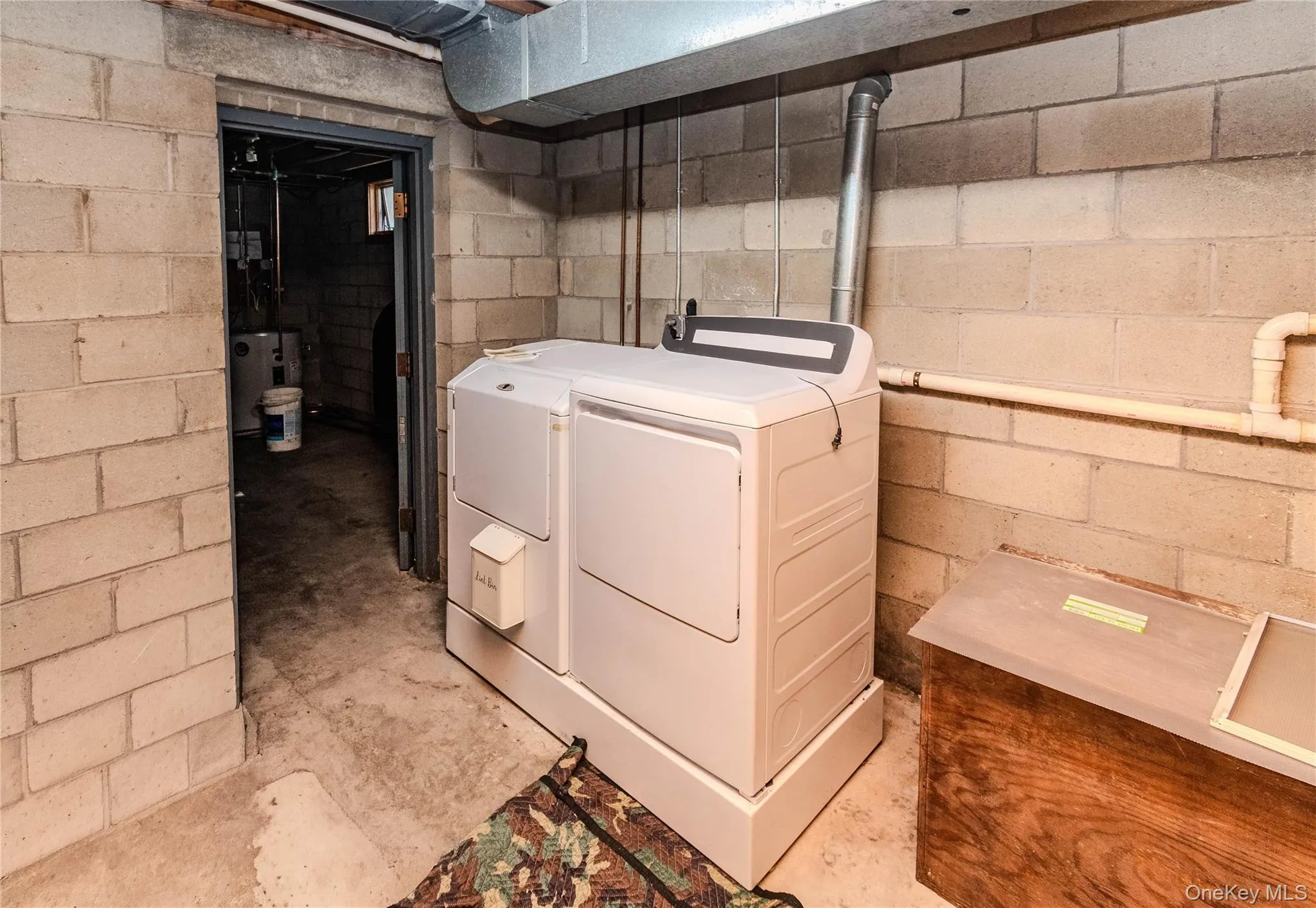 Laundry area featuring a side-by-side washer and dryer, concrete block walls, and exposed utility piping Laundry area featuring a side-by-side washer and dryer, concrete block walls, and exposed utility piping