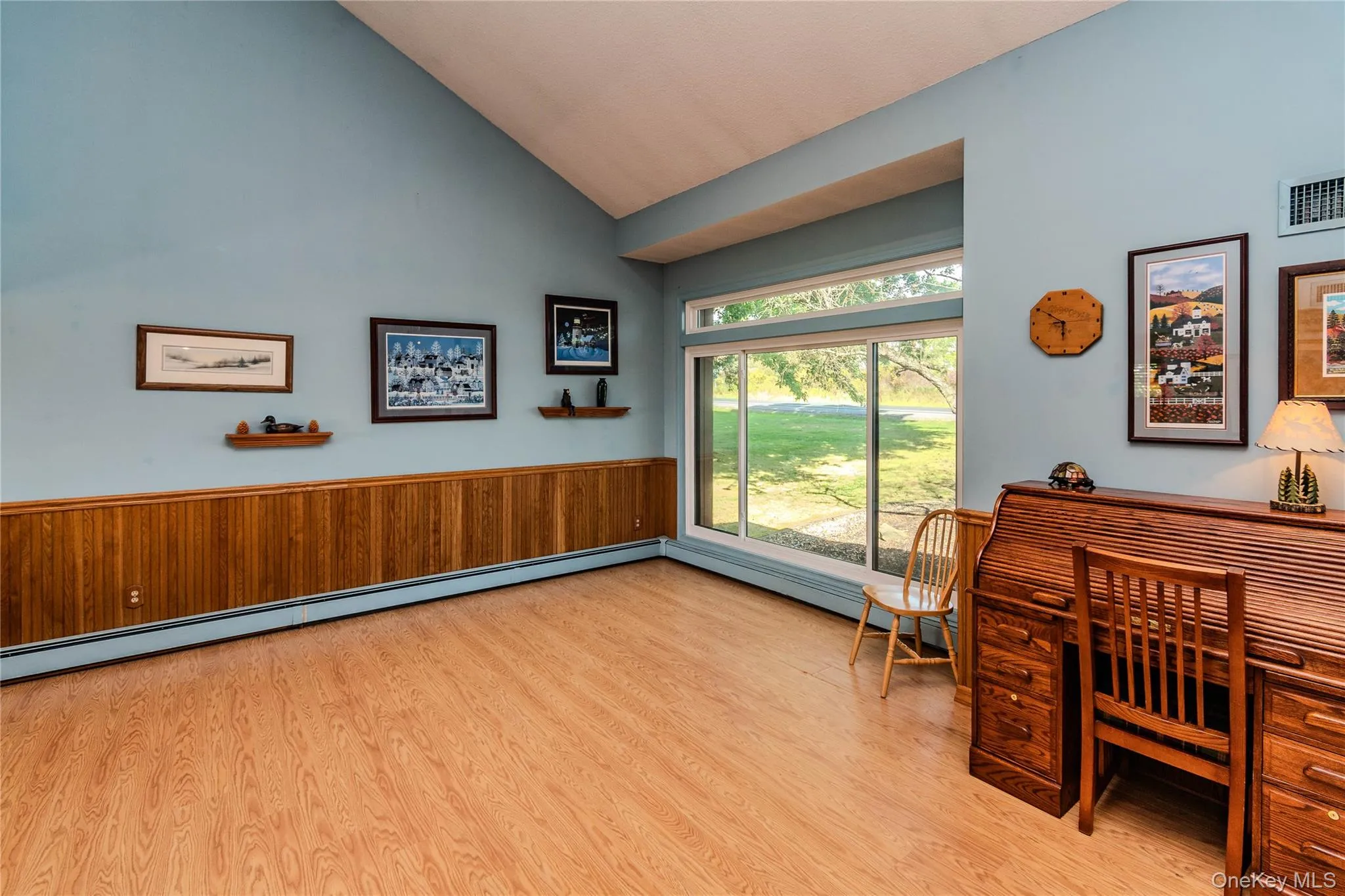 Vaulted ceiling, wood-finish flooring, wood paneling, large sliding glass windows, and built-in heat registers Vaulted ceiling, wood-finish flooring, wood paneling, large sliding glass windows, and built-in heat registers